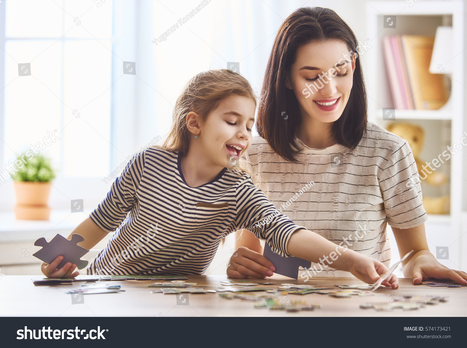 Happy family. Mother and daughter do puzzles together. Adult woman teaches child to solve puzzles. #574173421