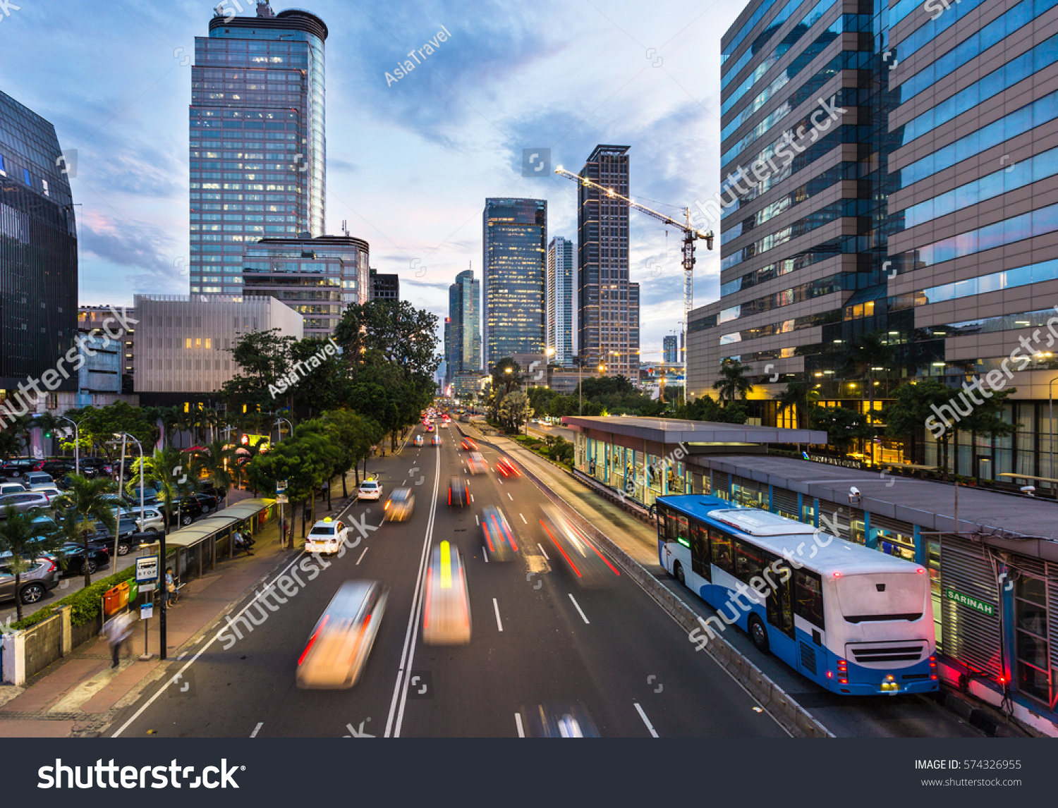 Traffic rushes in Jakarta business district along the city main avenue Jalan Thamrin at sunset in Indonesia capital city. The Transjakarta bus system enjoys its own traffic lane to avoid congestion. #574326955