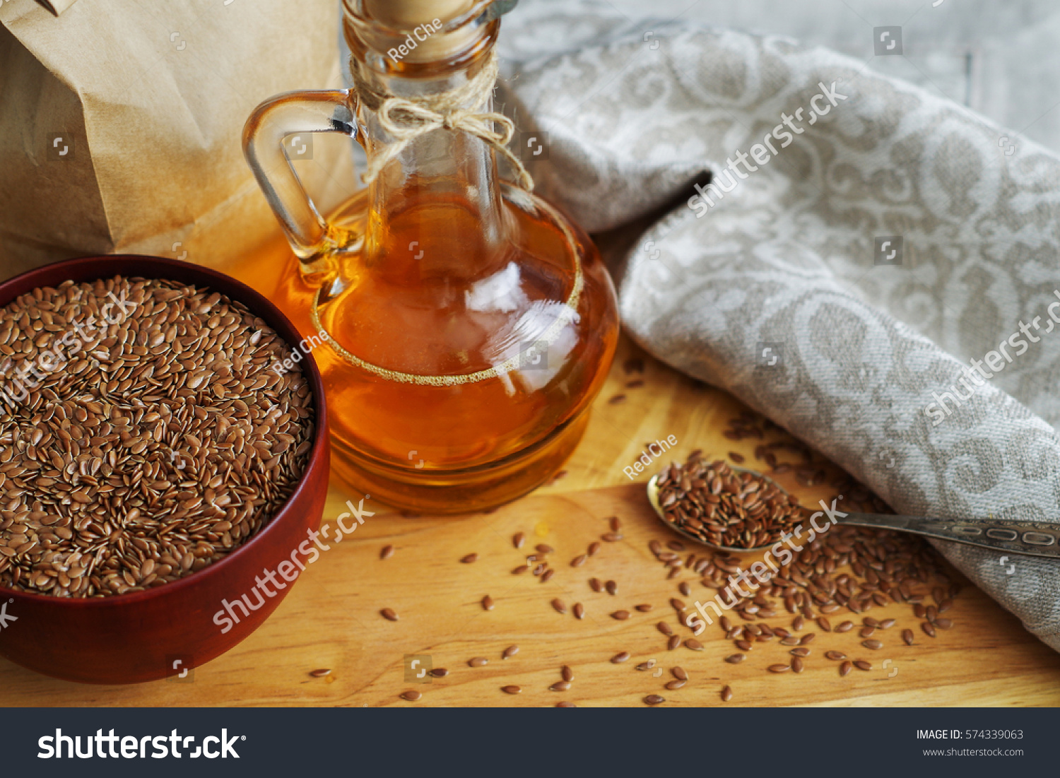 Flax seeds on spoon and in wooden bowl. Linseed oil in glass jug on wooden cutting board #574339063