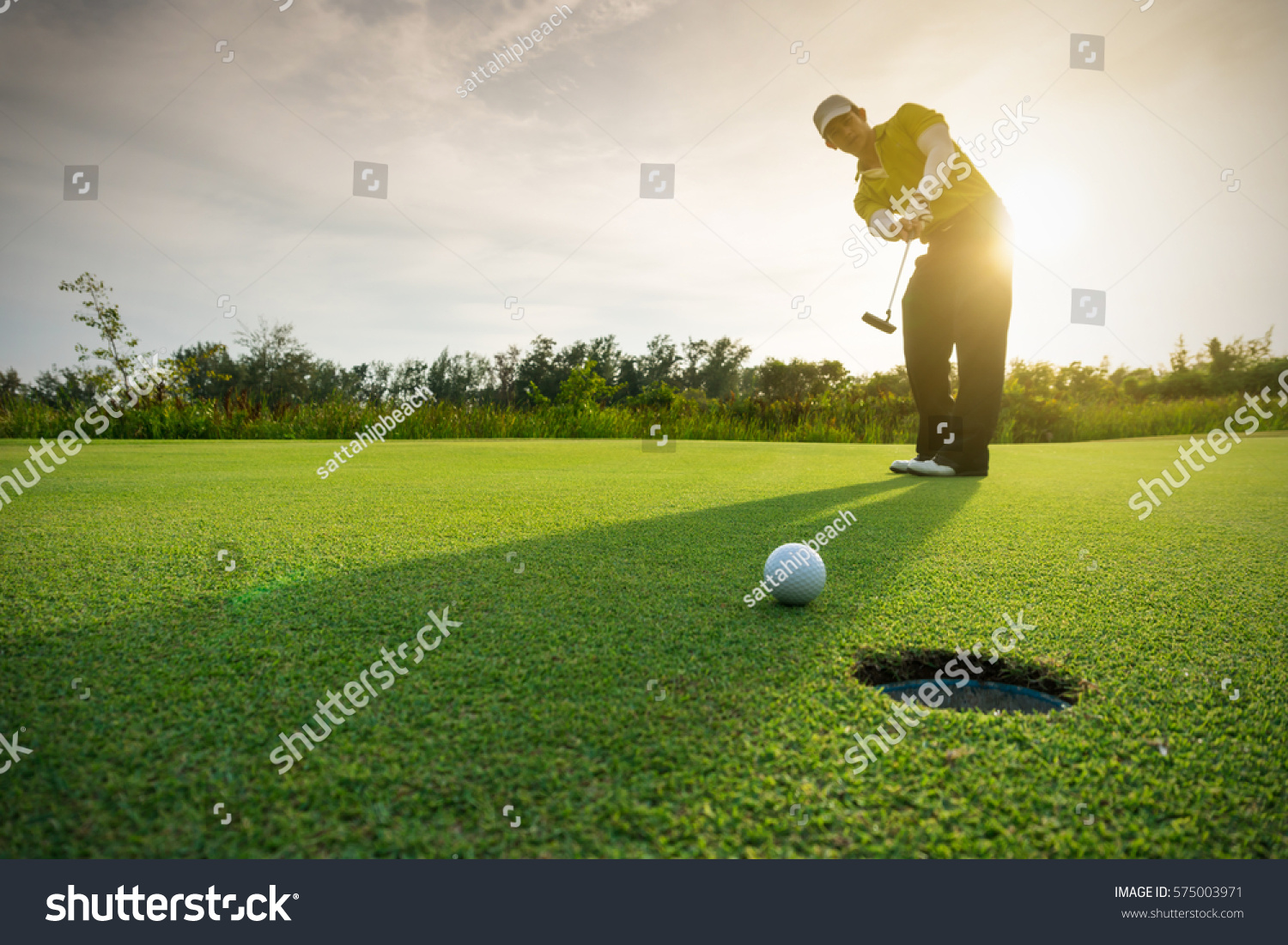 Golfer putting golf ball on the green golf, lens flare on sun set evening time. #575003971