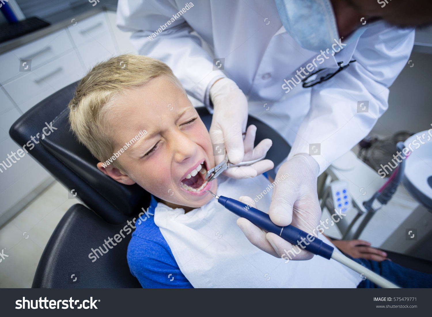 Dentist examining a young patient with tools at dental clinic #575479771