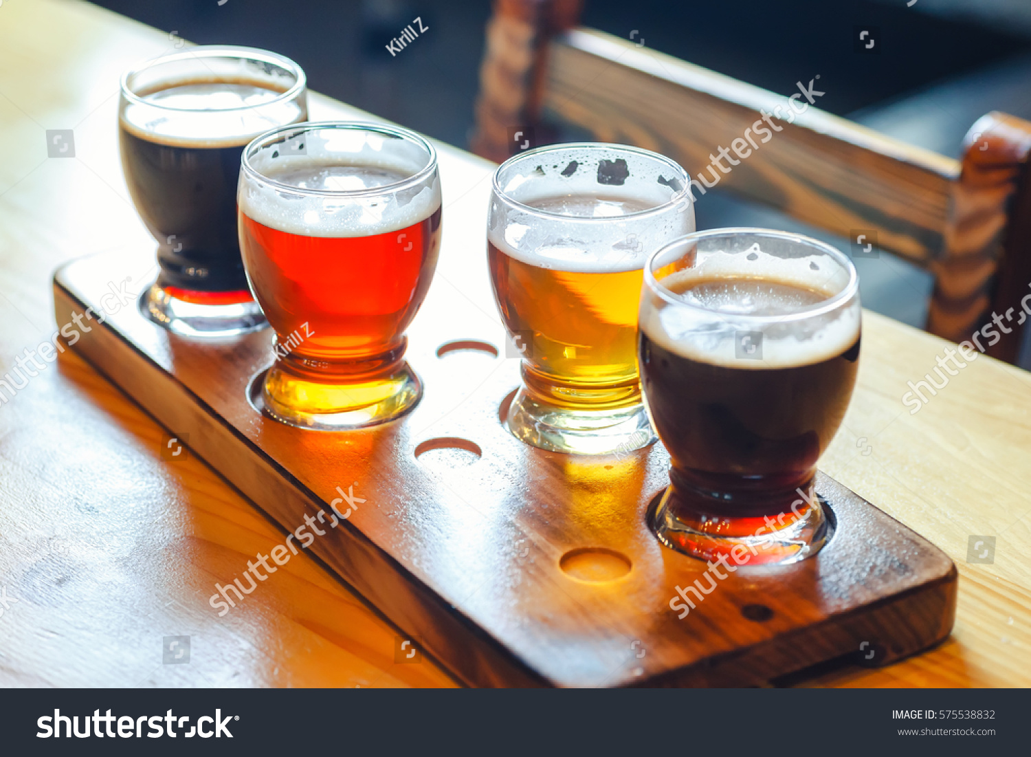 Flight with various types of craft beer in small glasses on a wooden table in a pub #575538832