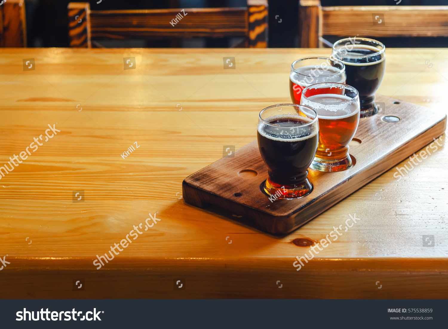 Flight with various types of craft beer in small glasses on a wooden table in a pub #575538859