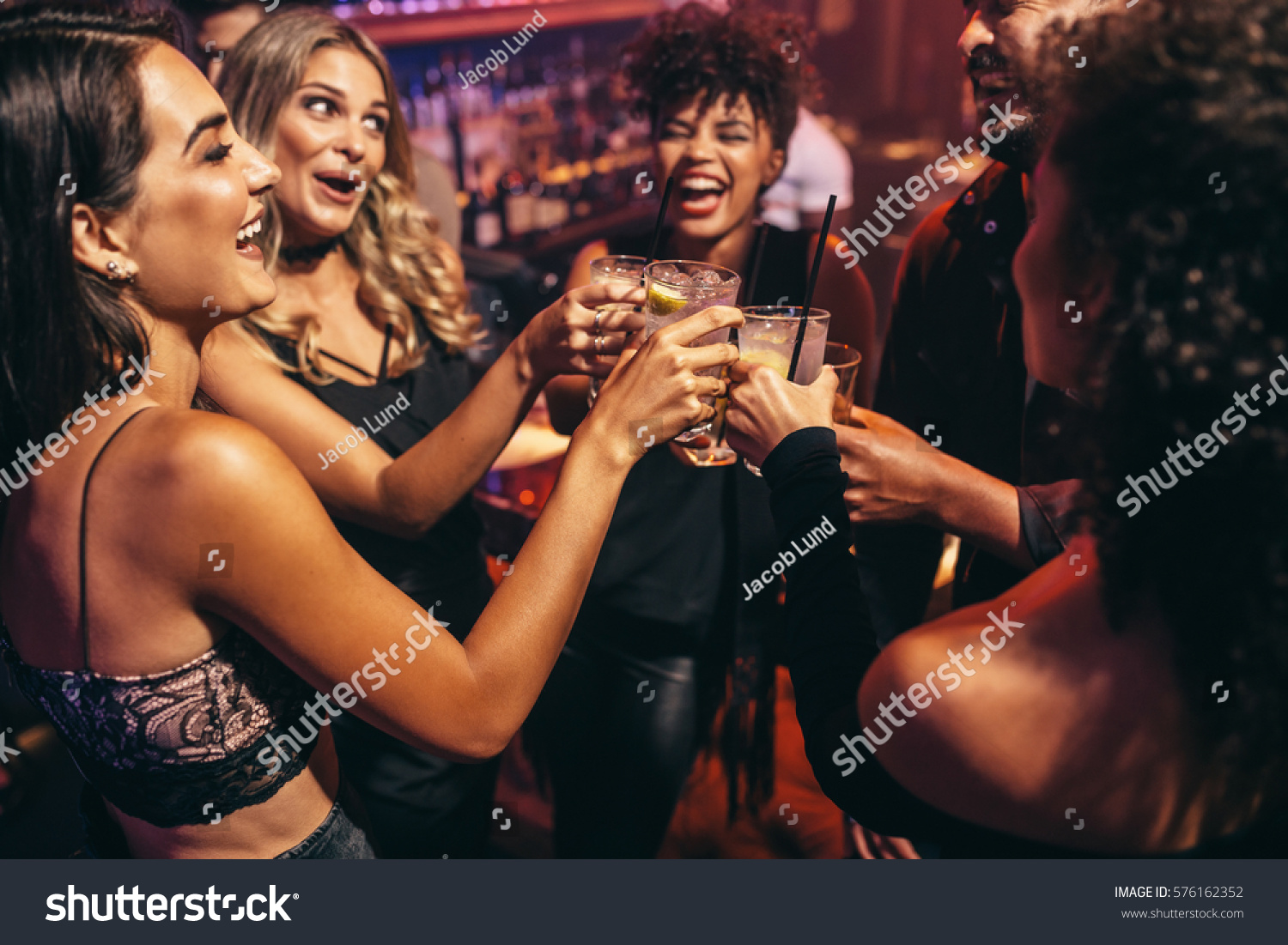 Group of friends partying in a nightclub and toasting drinks. Happy young people with cocktails at pub. #576162352