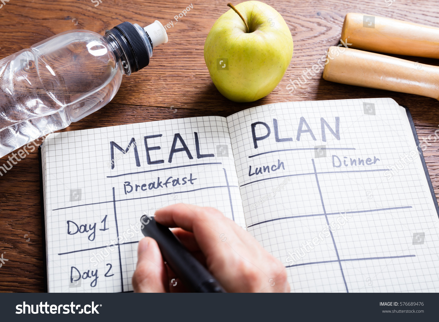 High Angle View Of A Person Hand Filling Meal Plan In Notebook At Wooden Desk #576689476