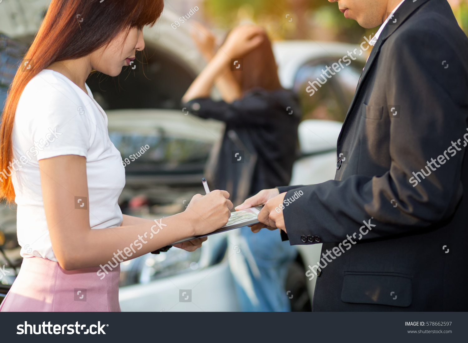 Side view of Asian woman writing on tablet while insurance agent examining car after accident,Insurance Concept #578662597