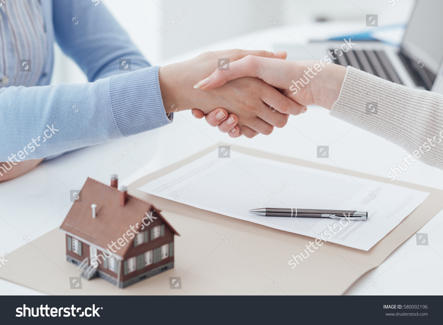 Real estate broker and customer shaking hands after signing a contract: real estate, home loan and insurance concept #580092196