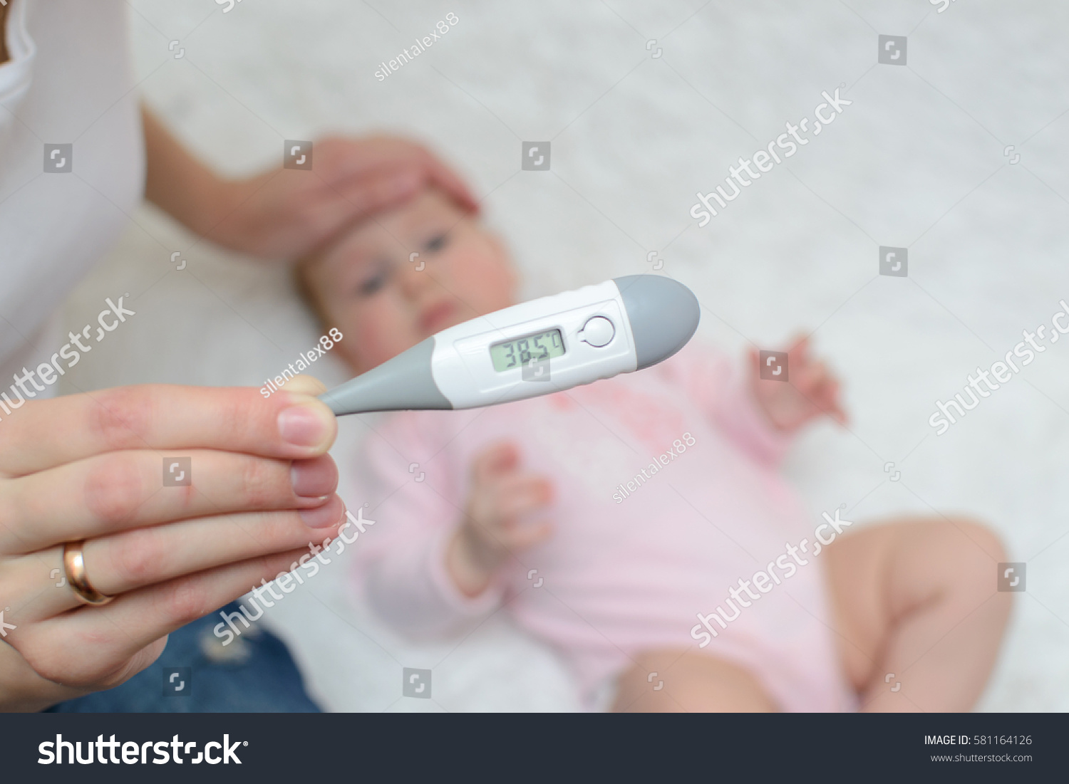 female hand holding a thermometer with high temperature on the background of a sick child #581164126