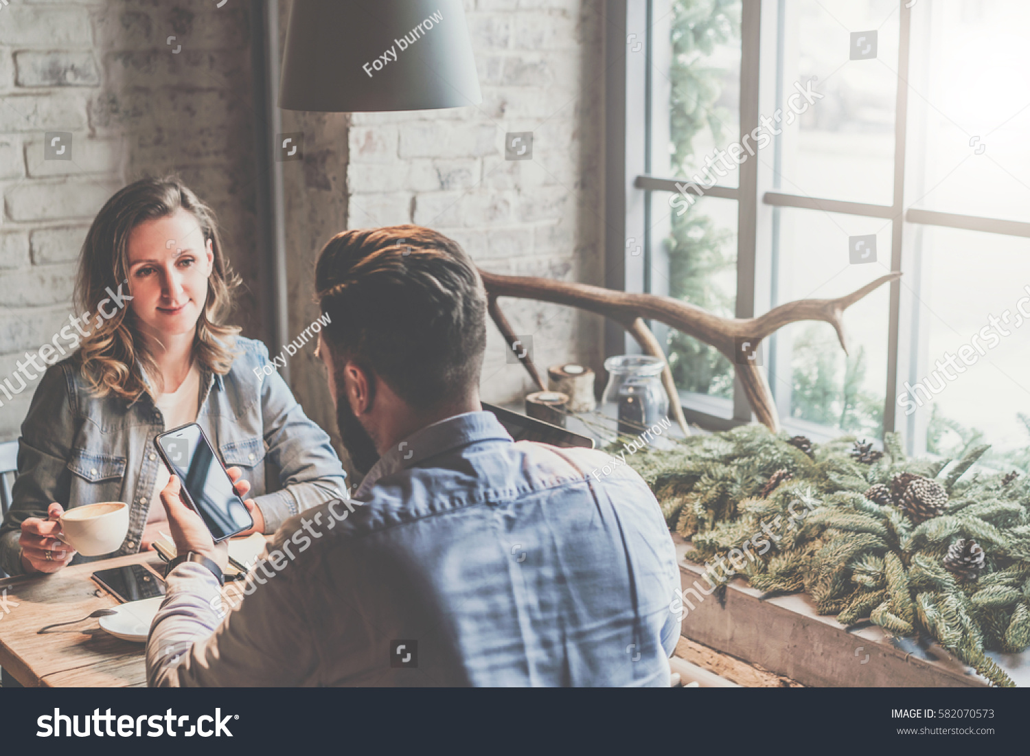 One-on-one meeting.Two young business people sitting at table in cafe.Businesswoman drinking coffee.Businessman using smartphone. Couple having dinner. Freelancers working. Teamwork, business meeting. #582070573