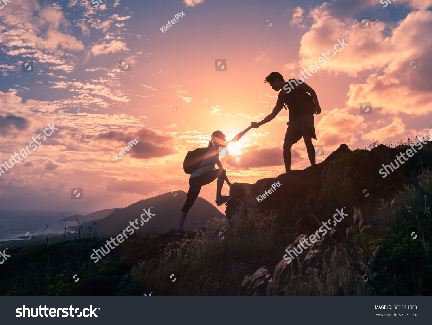 People helping each other hike up a mountain at sunrise.  Giving a helping hand, and active fit lifestyle concept. #582394888