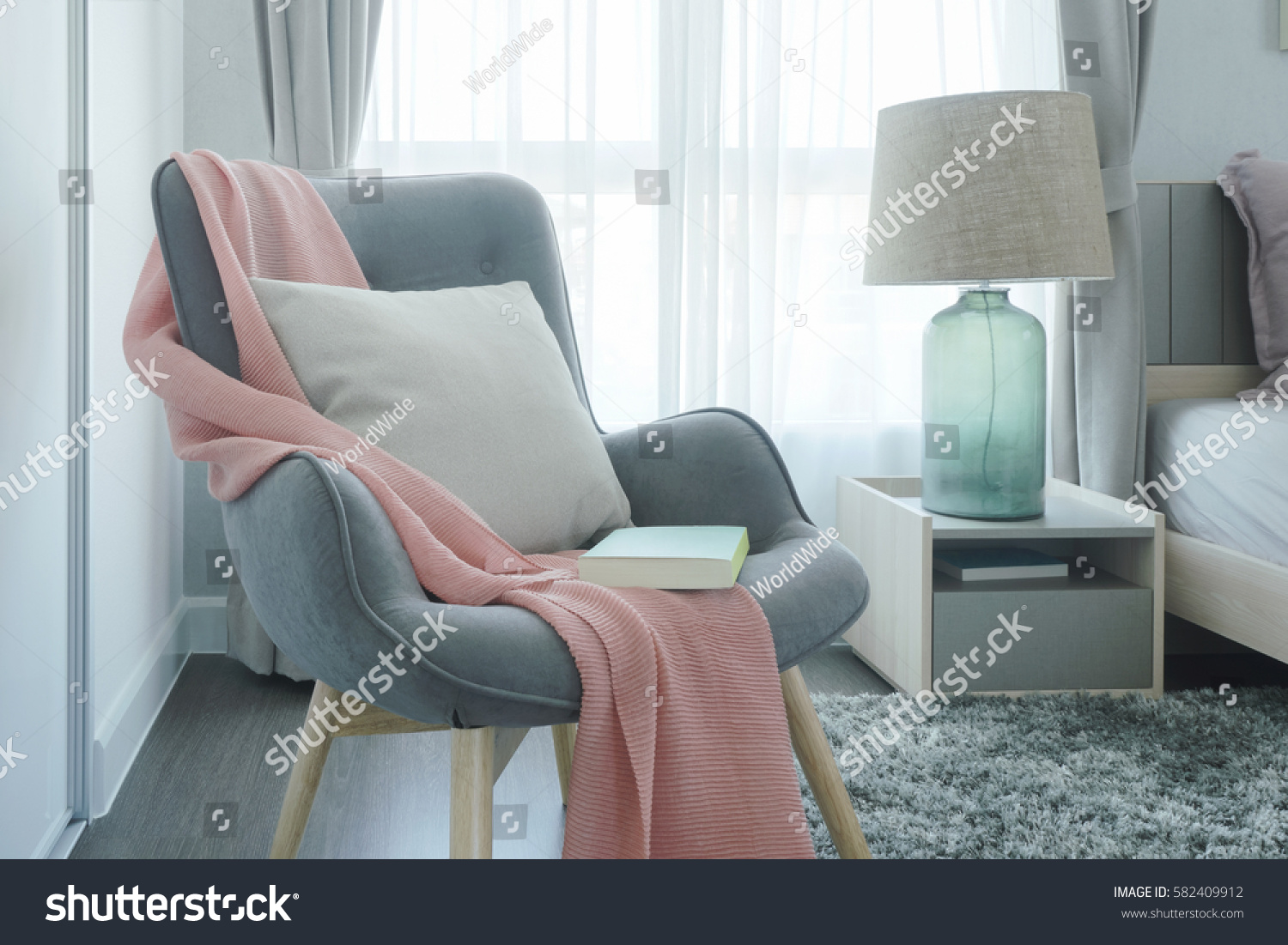 Gray easy armchair with pink scarf, pillow and book next to bed in the bedroom #582409912