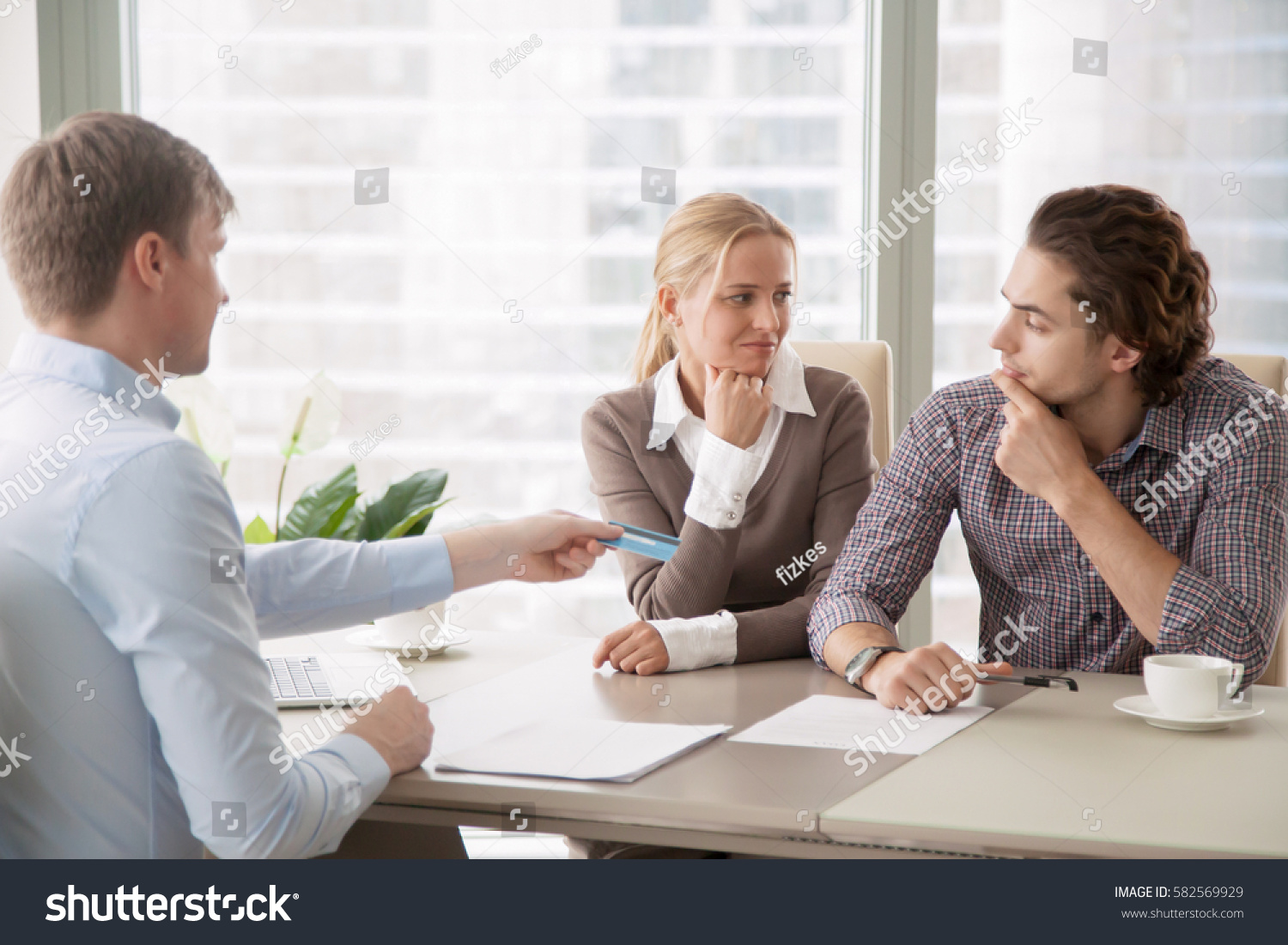 Bank consultant trying to convince clients to get a loan, offering credit card with high interest rate. Middle-class family sorting out finances and budget, not sure in the choice, looking doubtful  #582569929