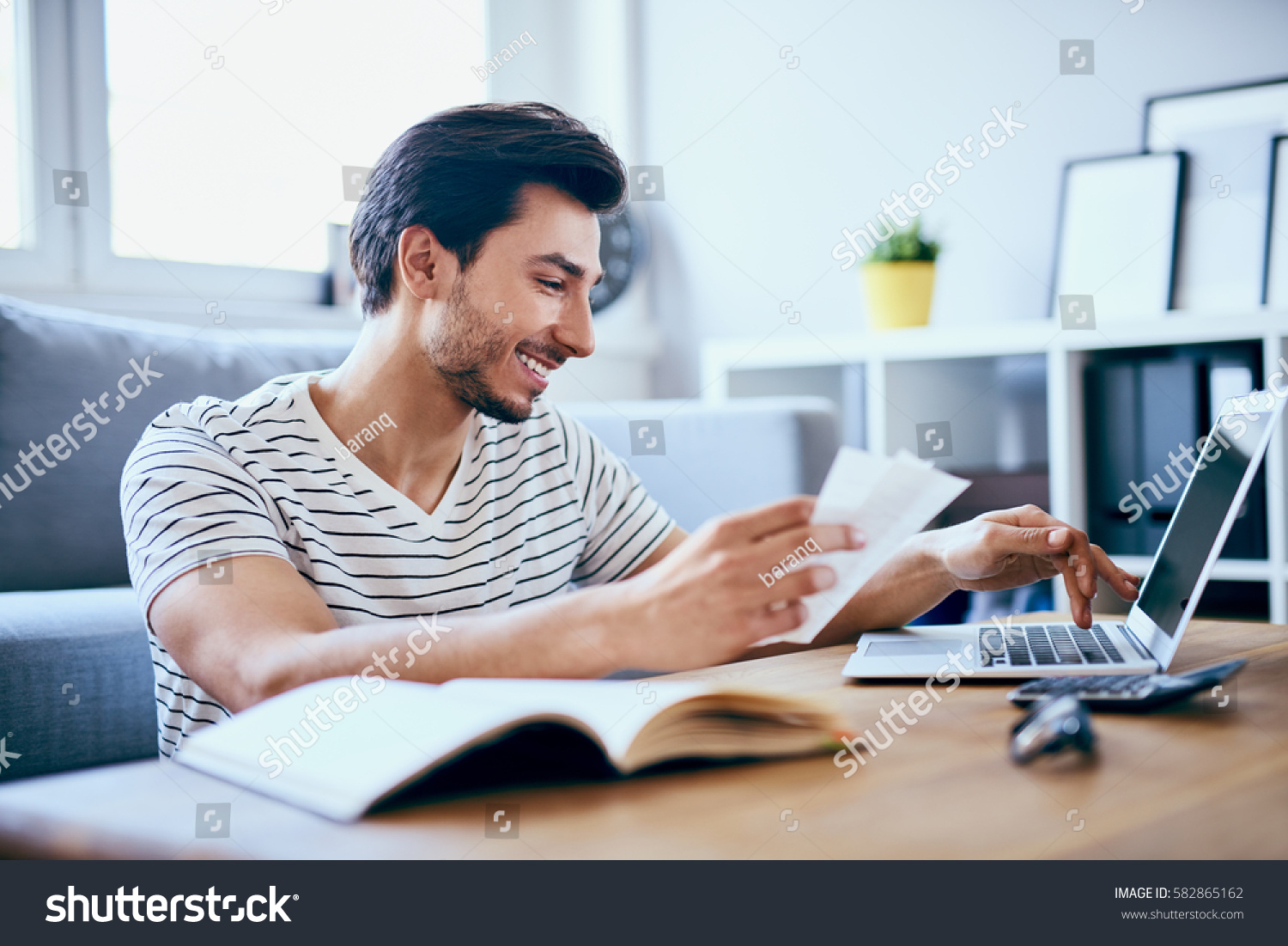 Happy man paying bills on his laptop in living room #582865162