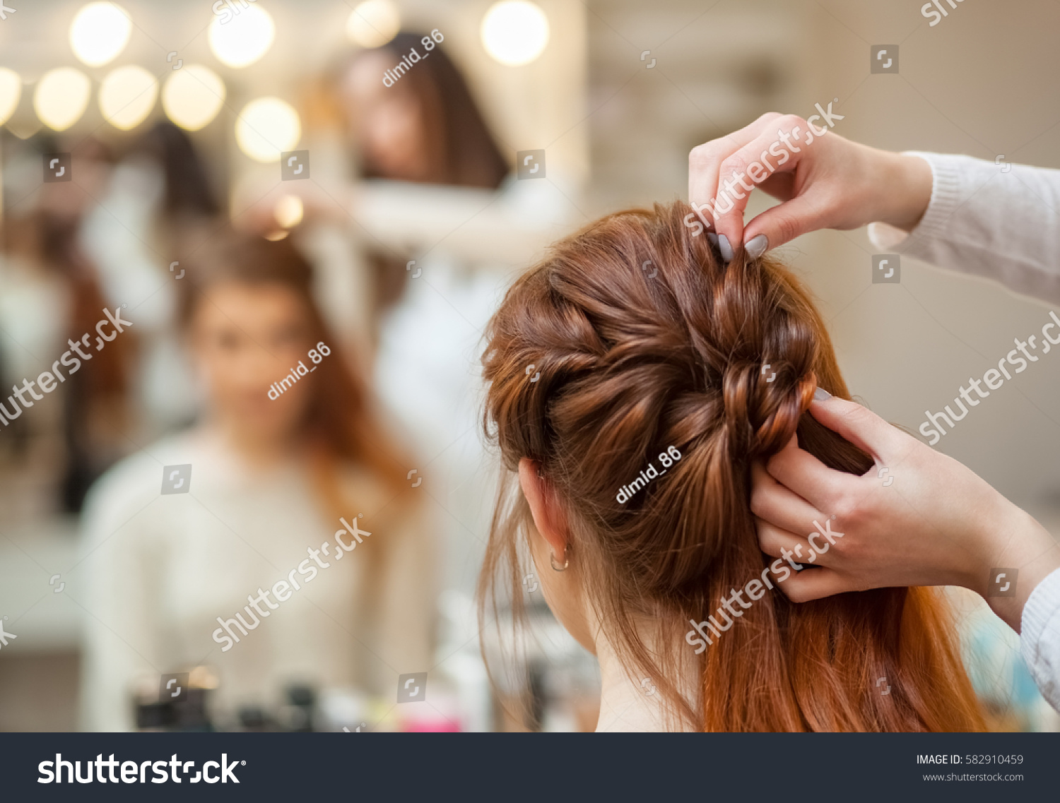 Beautiful, red-haired girl with long hair, hairdresser weaves a French braid, in a beauty salon. Professional hair care and creating hairstyles. #582910459