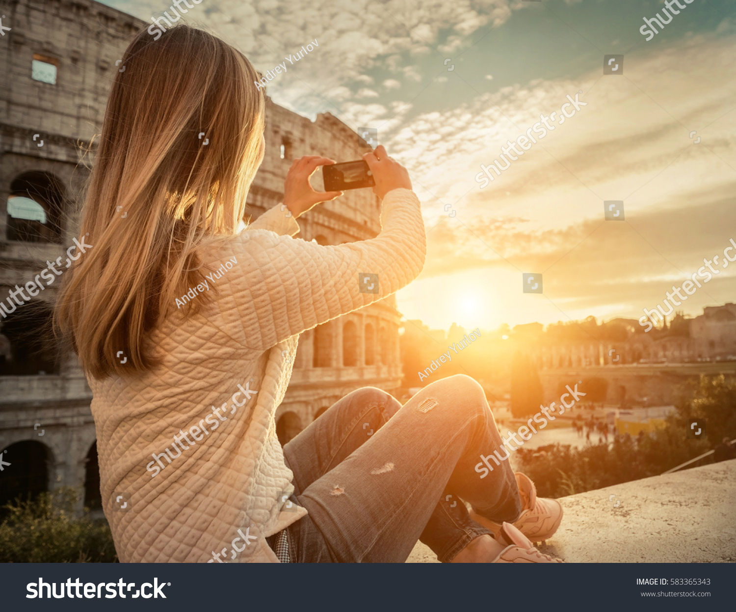 Woman tourist selfie with phone camera in hands near the Coliseum in Rome under sunlight and blue sky. Famous popular touristic place in the world. #583365343