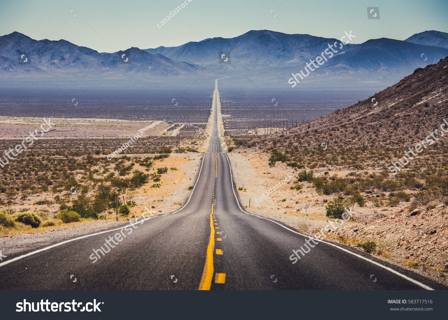 Classic panorama view of an endless straight road running through the barren scenery of the American Southwest with extreme heat haze on a beautiful hot sunny day with blue sky in summer #583717516