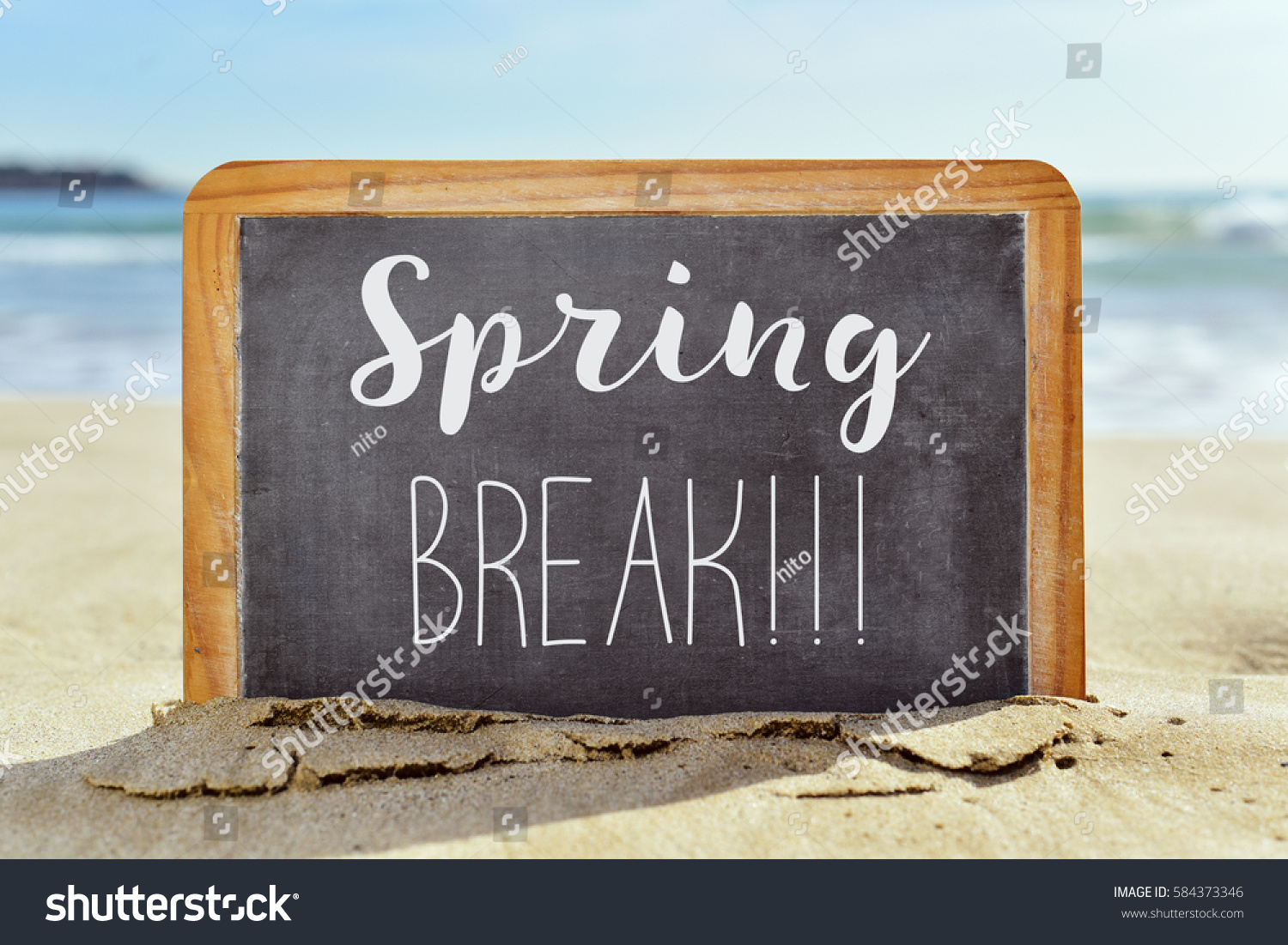 closeup of a wooden-framed chalkboard with the text spring break written in it, on the sand of a lonely beach #584373346