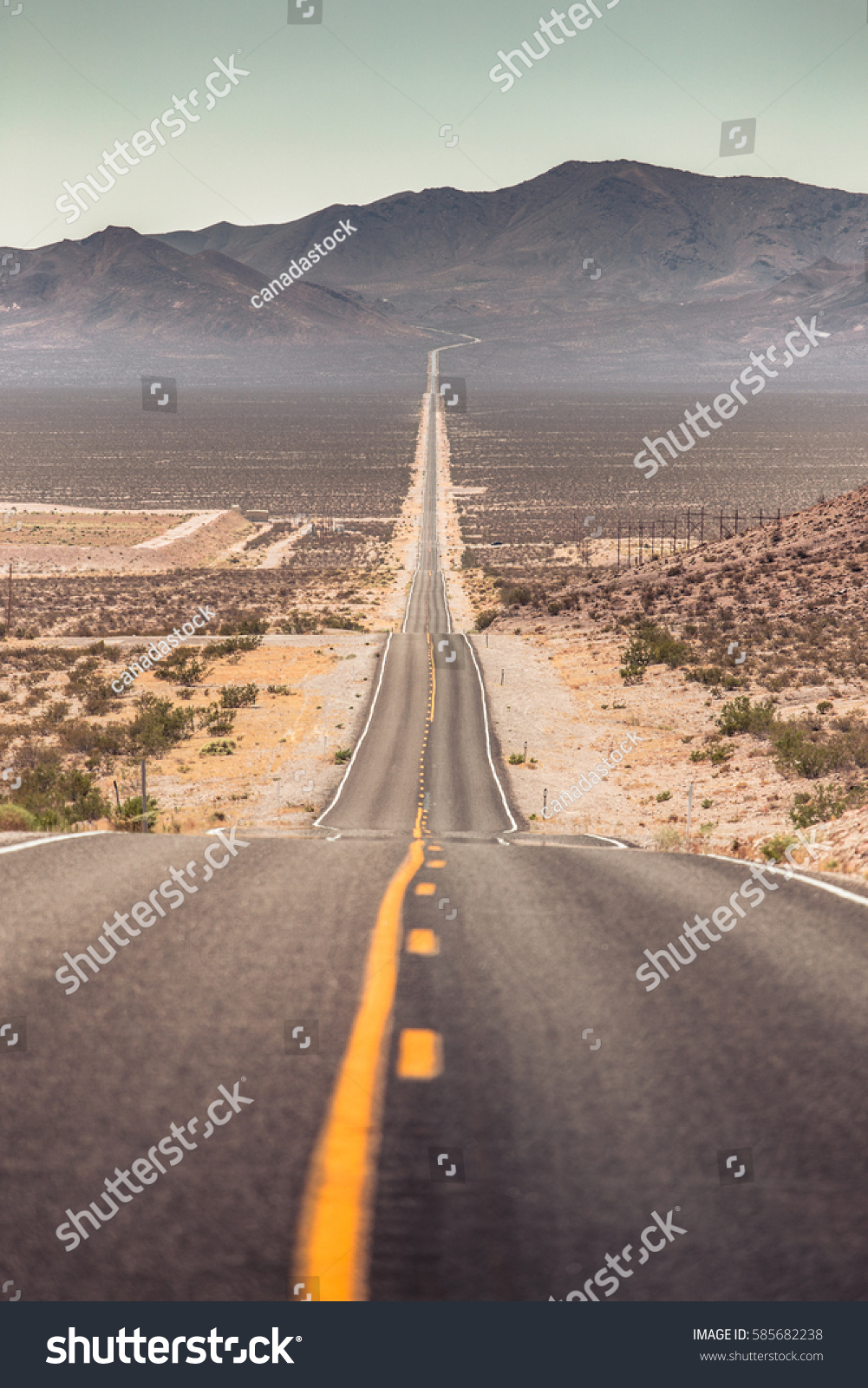 Classic panorama view of an endless straight road running through the barren scenery of the American Southwest with extreme heat haze on a beautiful hot sunny day with blue sky in summer #585682238