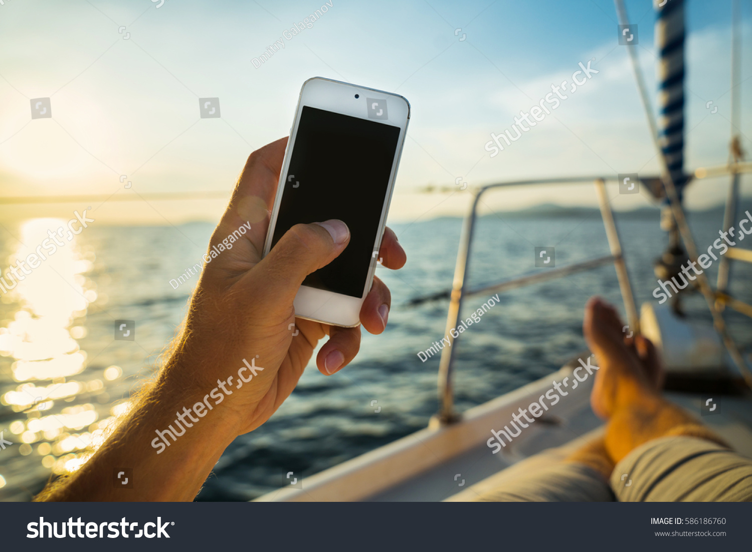 Summer leisure. Rest on a yacht with a phone in his hand. Man lying on the deck and enjoy your smartphone. The guy doing the photo feet on the background seascape and yachts. #586186760