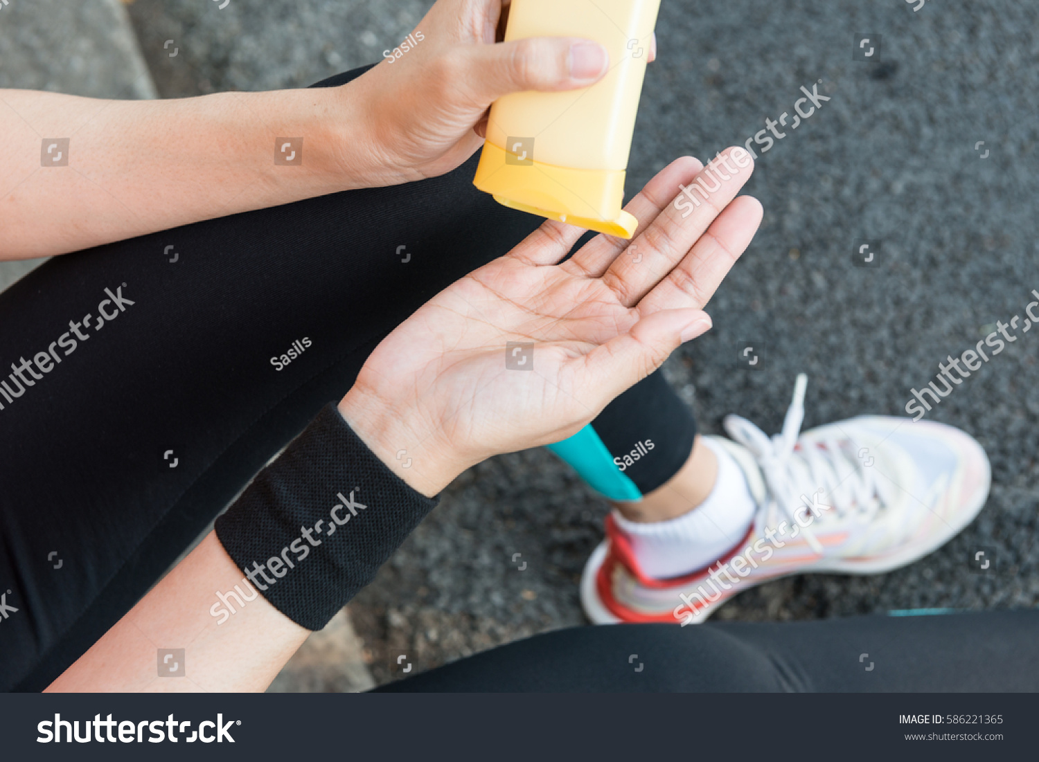 Young Asian female runner sitting down putting lotion on hand and arm ready for running exercise in the morning for healthy sport running exercise summer spring skincare sunny day concepts #586221365