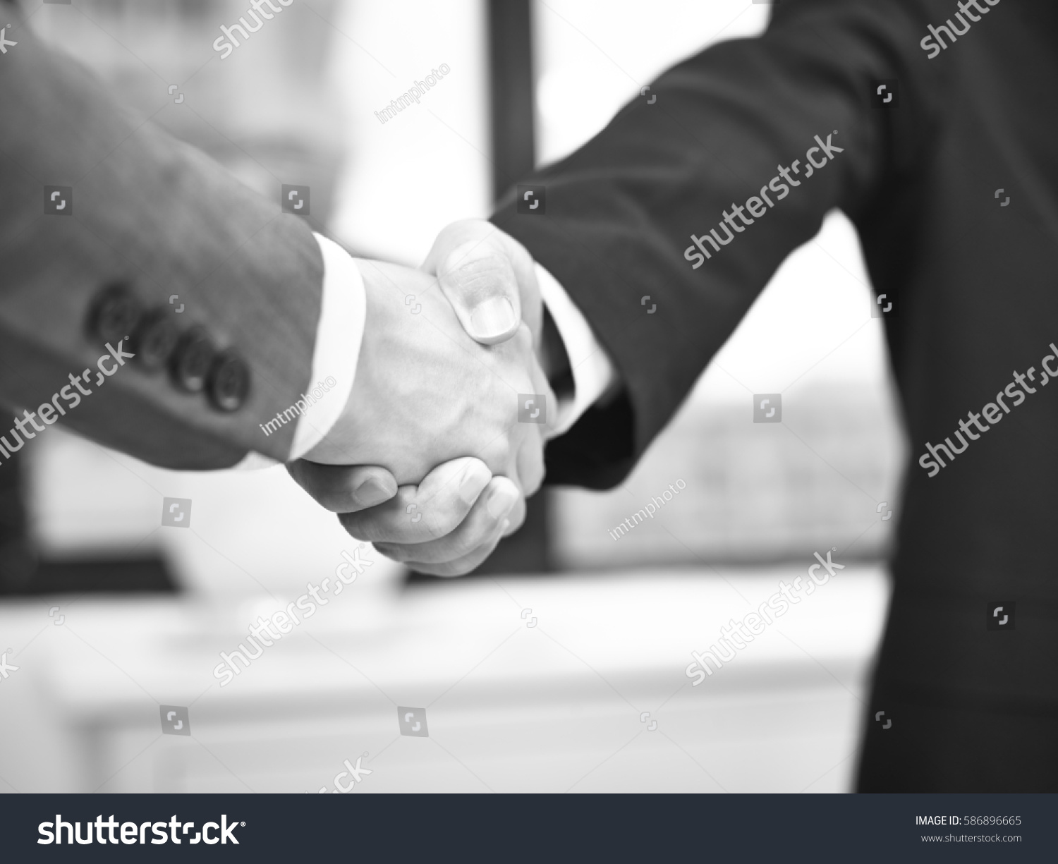 two corporate businessmen shaking hands in office, black and white. #586896665