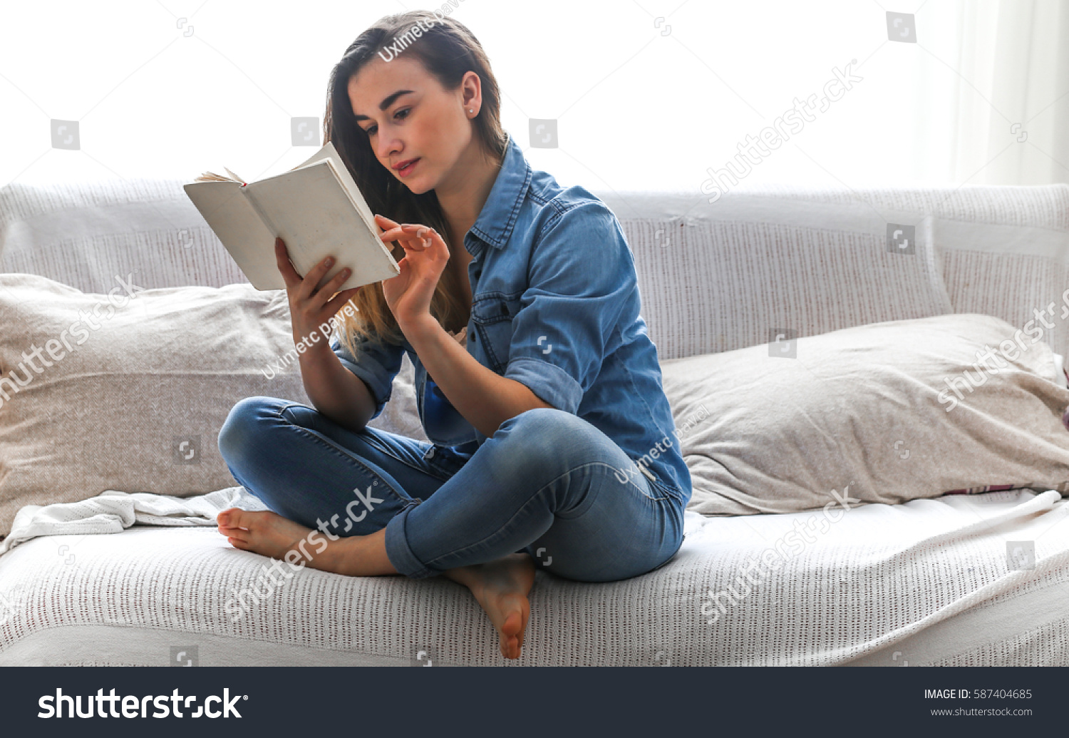White cozy bed and a beautiful girl, reading a book, concepts of home and comfort, place for text #587404685