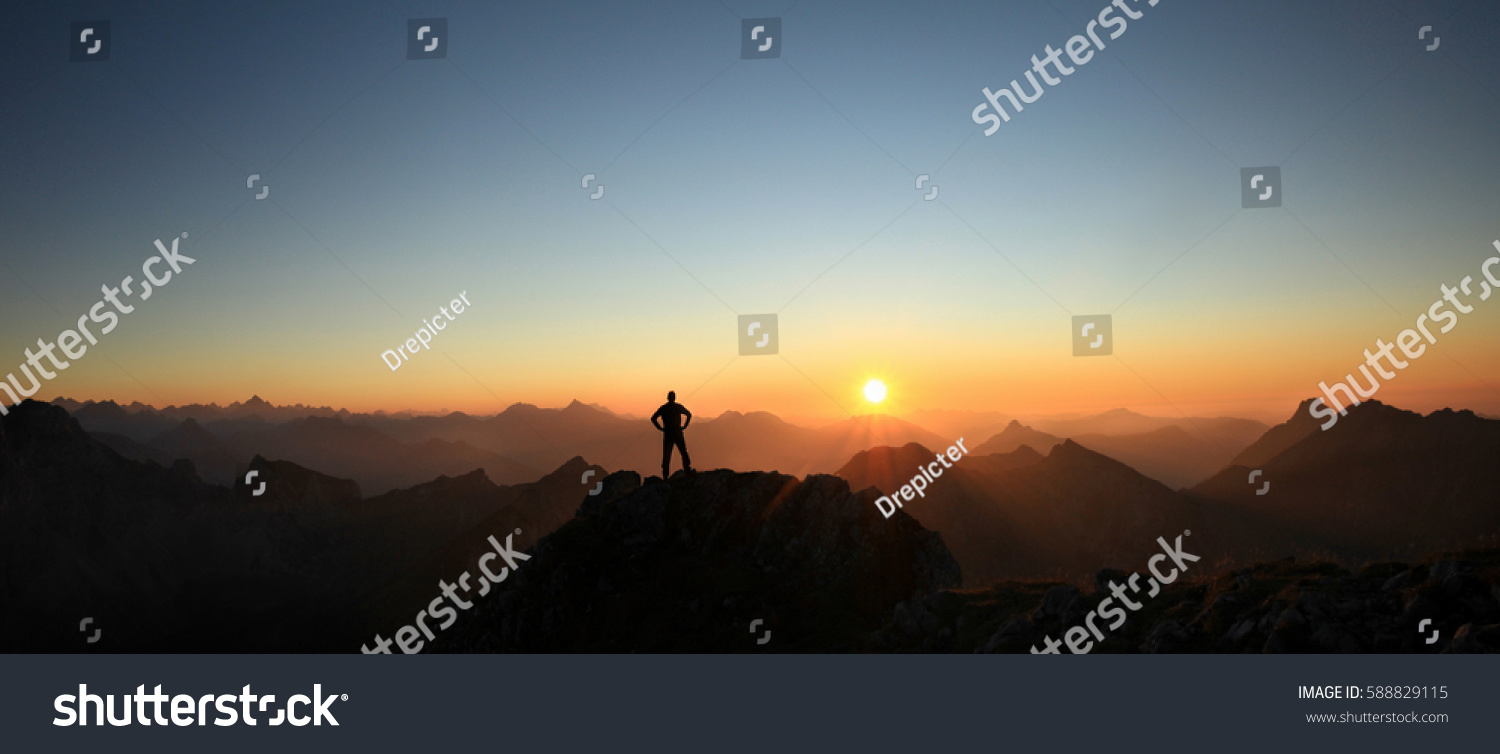 Man reaching summit enjoying freedom and looking towards mountains sunset. #588829115
