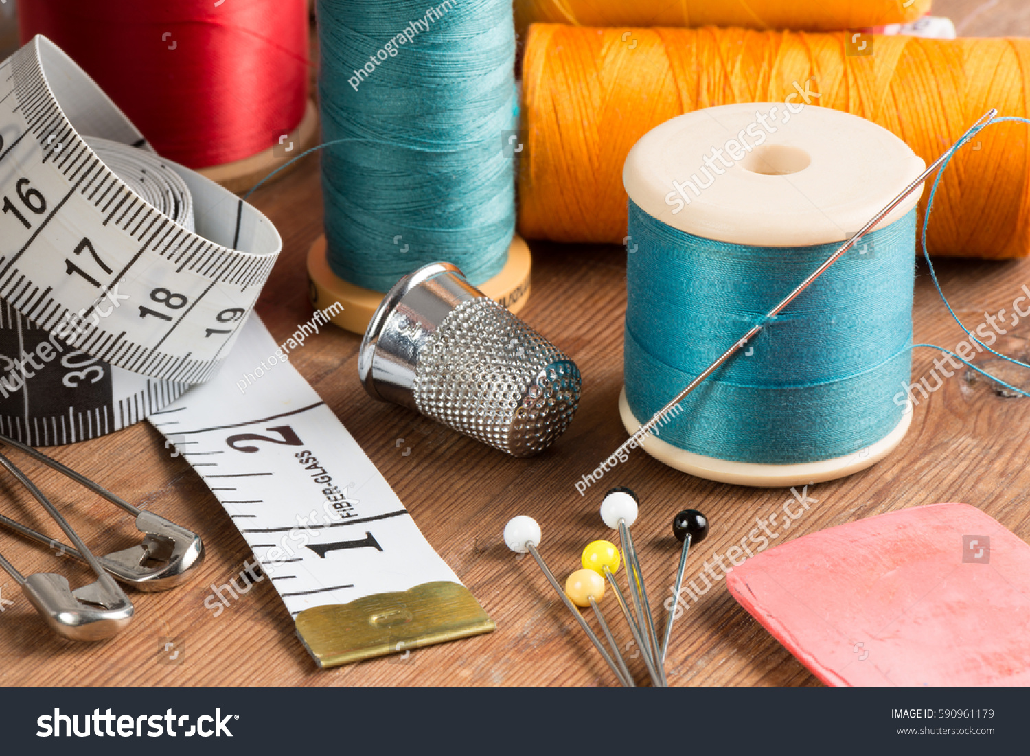Spools of thread and basic sewing tools including pins, needle, a thimble, and tape measure on a wooden tabletop #590961179