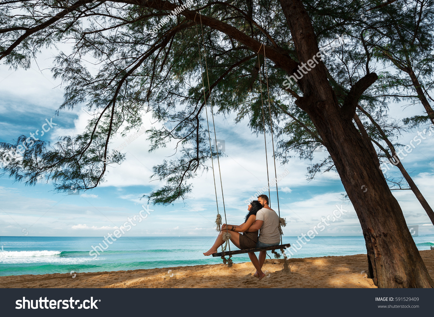Couple in love on a swing by the sea. Couple in love on an island off the coast. Honeymoon. Couple by the sea. Man and woman travel to beautiful places. Honeymoon trip. Relax on the island. In love #591529409