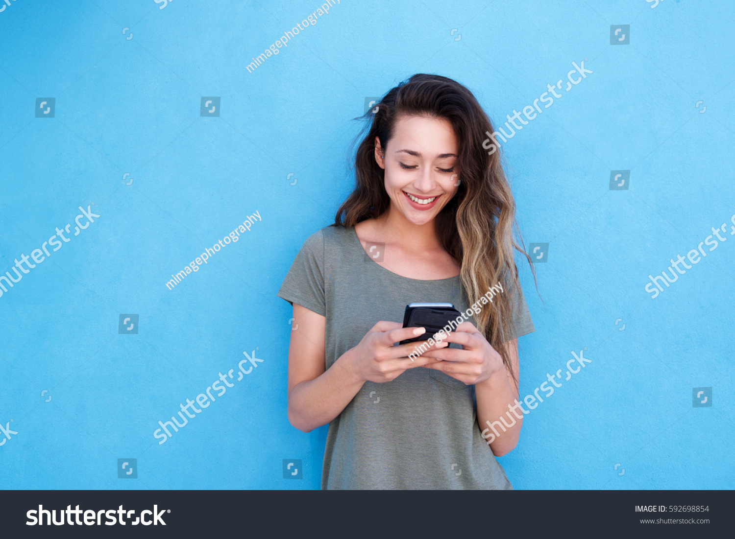 Front portrait of young smiling woman using mobile phone against blue background #592698854