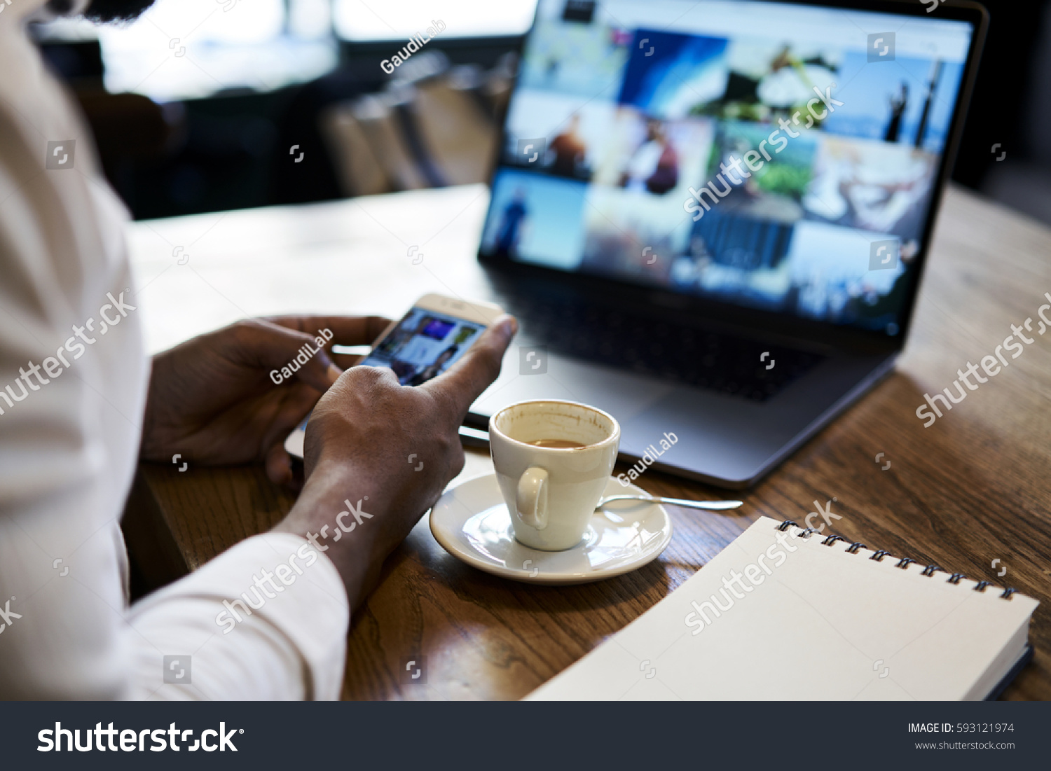 Cropped image of man's hand holding modern smartphone while sending multimedia files to laptop computer editing before publish with mock up screen connected to free wireless internet in coffee shop #593121974