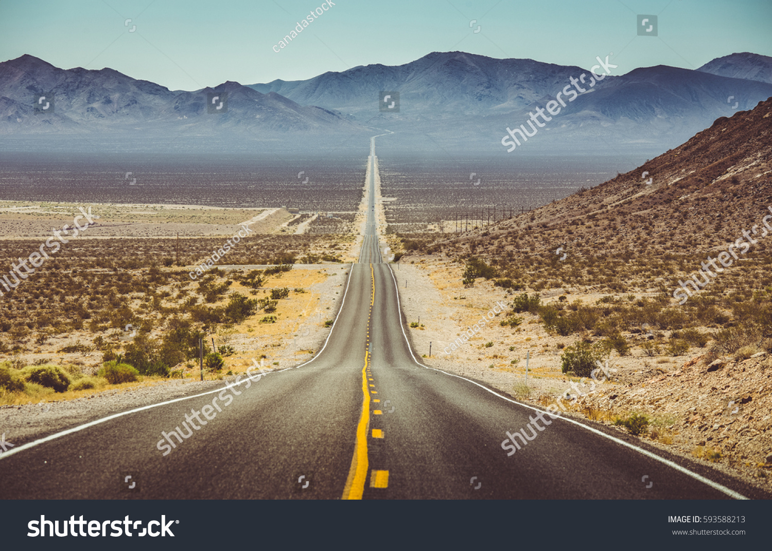 Classic vertical panorama view of an endless straight road running through the barren scenery of the American Southwest with extreme heat haze on a beautiful hot sunny day with blue sky in summer #593588213