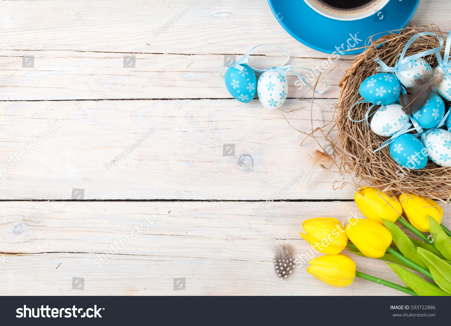 Easter background with blue and white eggs in nest, yellow tulips and coffee cup over white wood. Top view with copy space #593722886