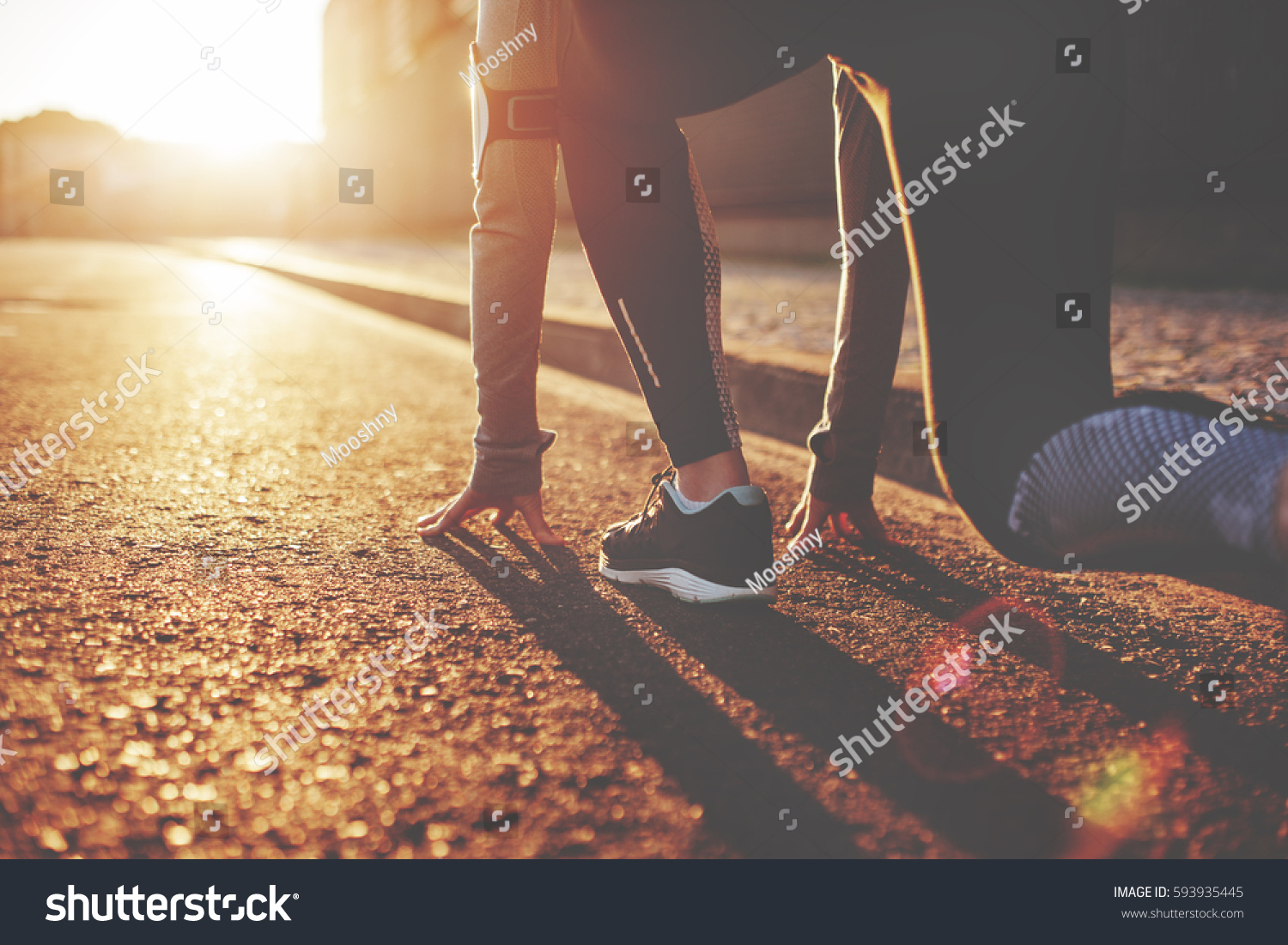 Athlete woman in running start pose on the city street. Sport tight clothes. Bright sunset, blurry background. Horizontal #593935445