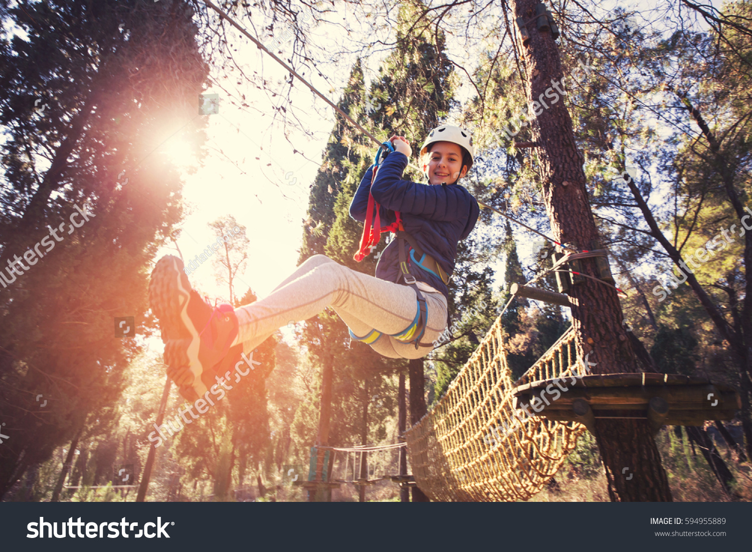 Happy school girl enjoying activity in a climbing adventure park on a summer day #594955889