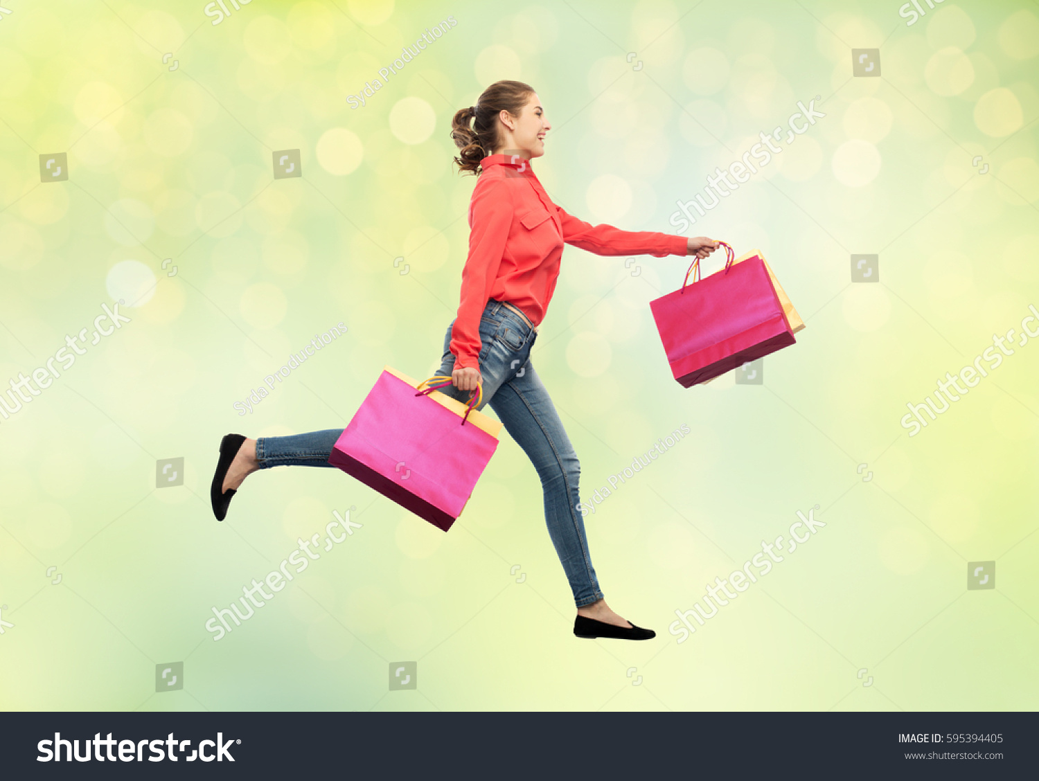 sale, motion and people concept - smiling young woman with shopping bags running in air over summer green lights background #595394405