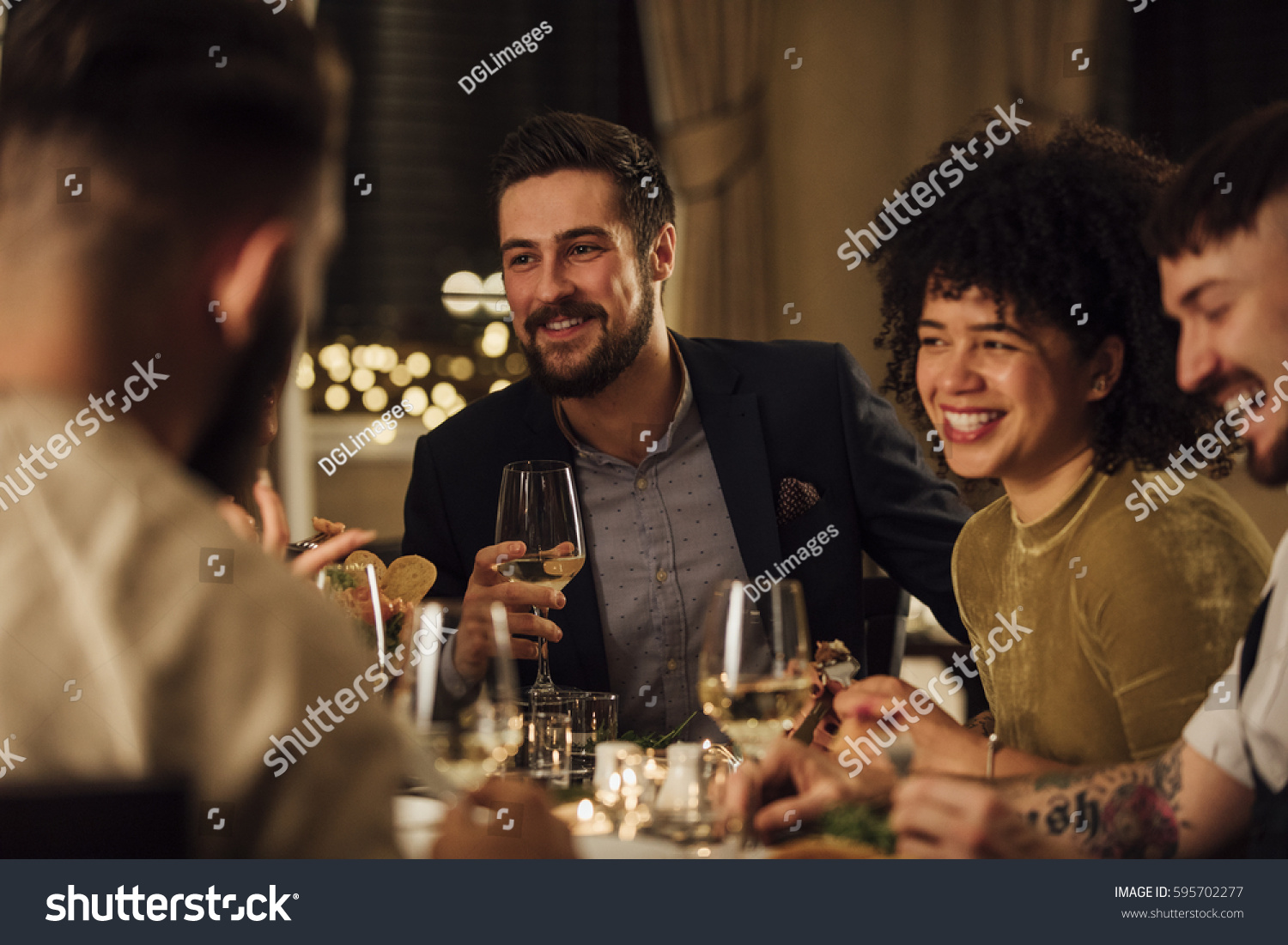 Group of friends are enjoying a meal in a restaurant. They are are talking and laughing while eating and drinking wine. #595702277