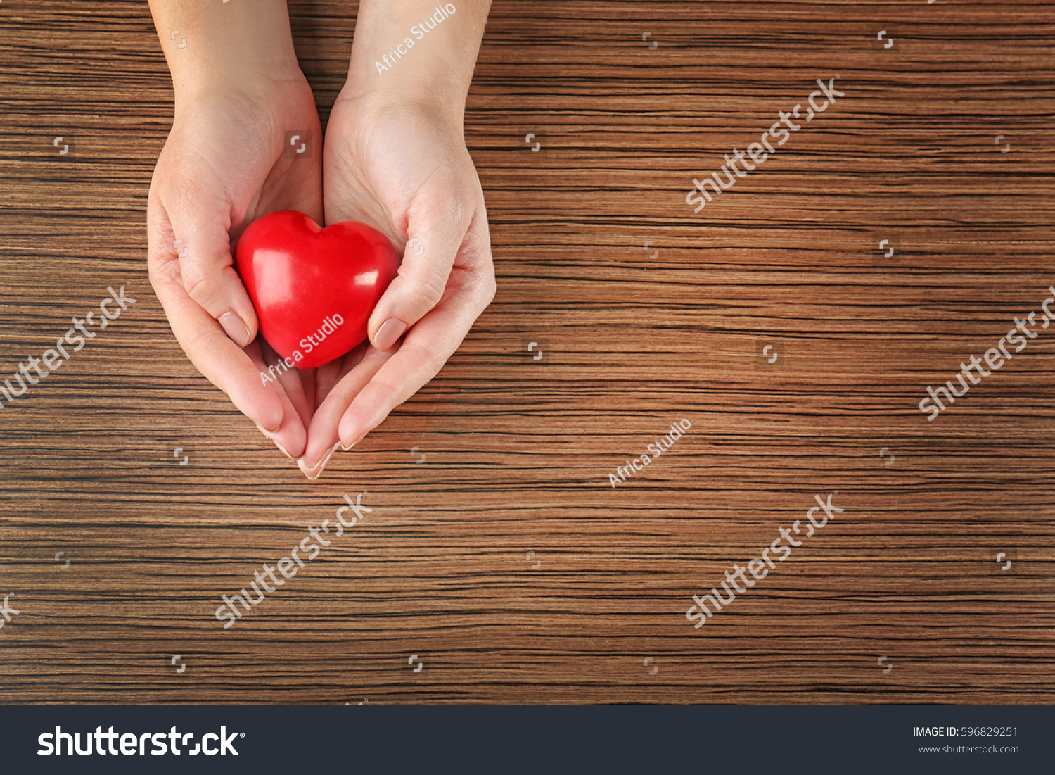 Female hands holding red heart on wooden background #596829251