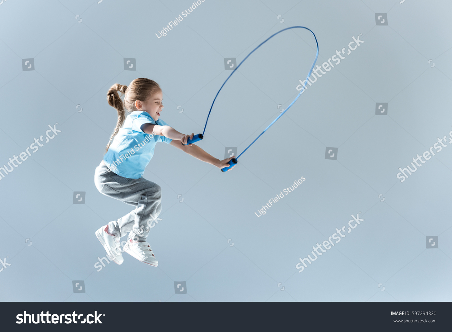side view of happy girl humping exercising with skipping rope isolated on grey #597294320