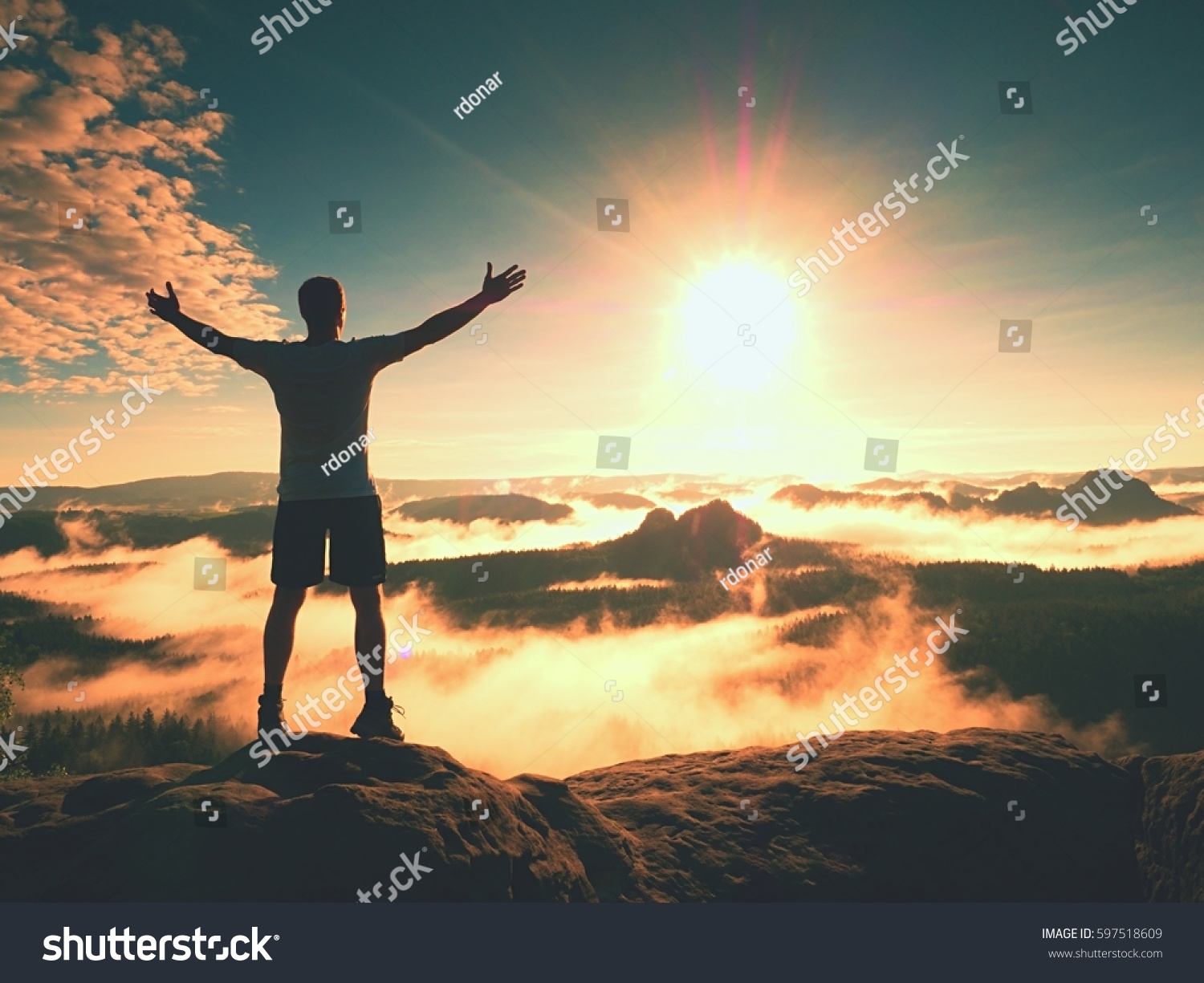 Happy man gesture of triumph with rams in air. Funny hiker on peak of sandstone rock in national park Saxony Switzerland watching to horizon #597518609