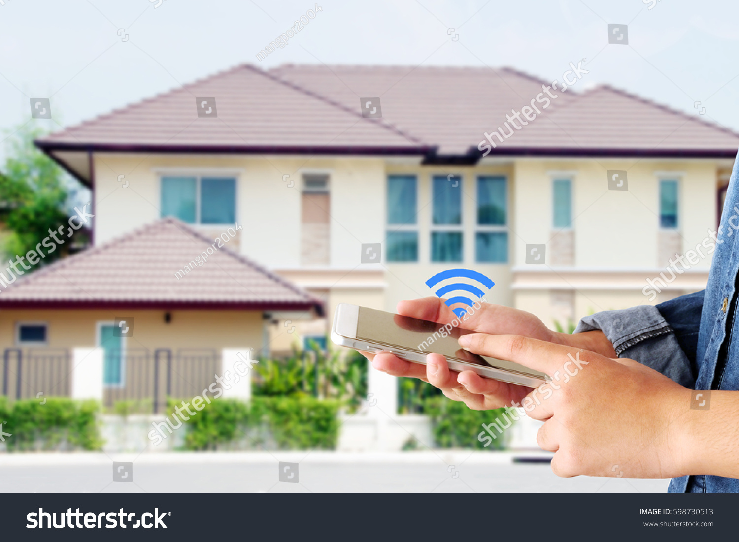 Hand holding smart phone over wifi icon and blur house background, smart home control concept #598730513