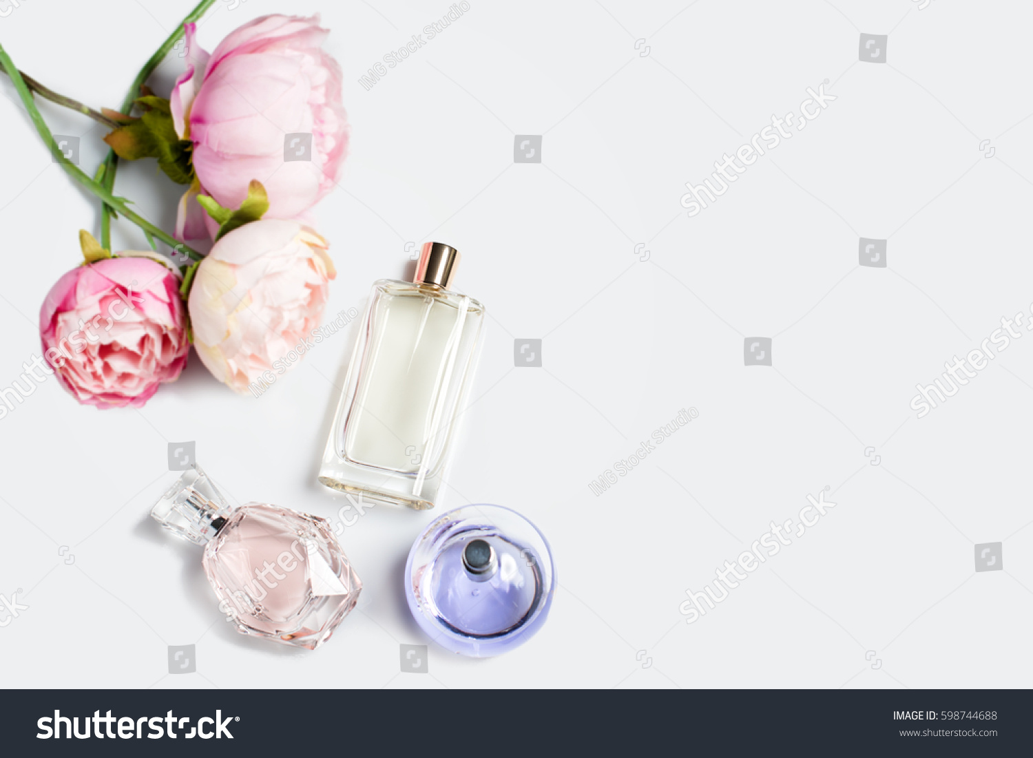 Perfume bottles with flowers on light background. Perfumery, cosmetics, fragrance collection. Free space for text. #598744688