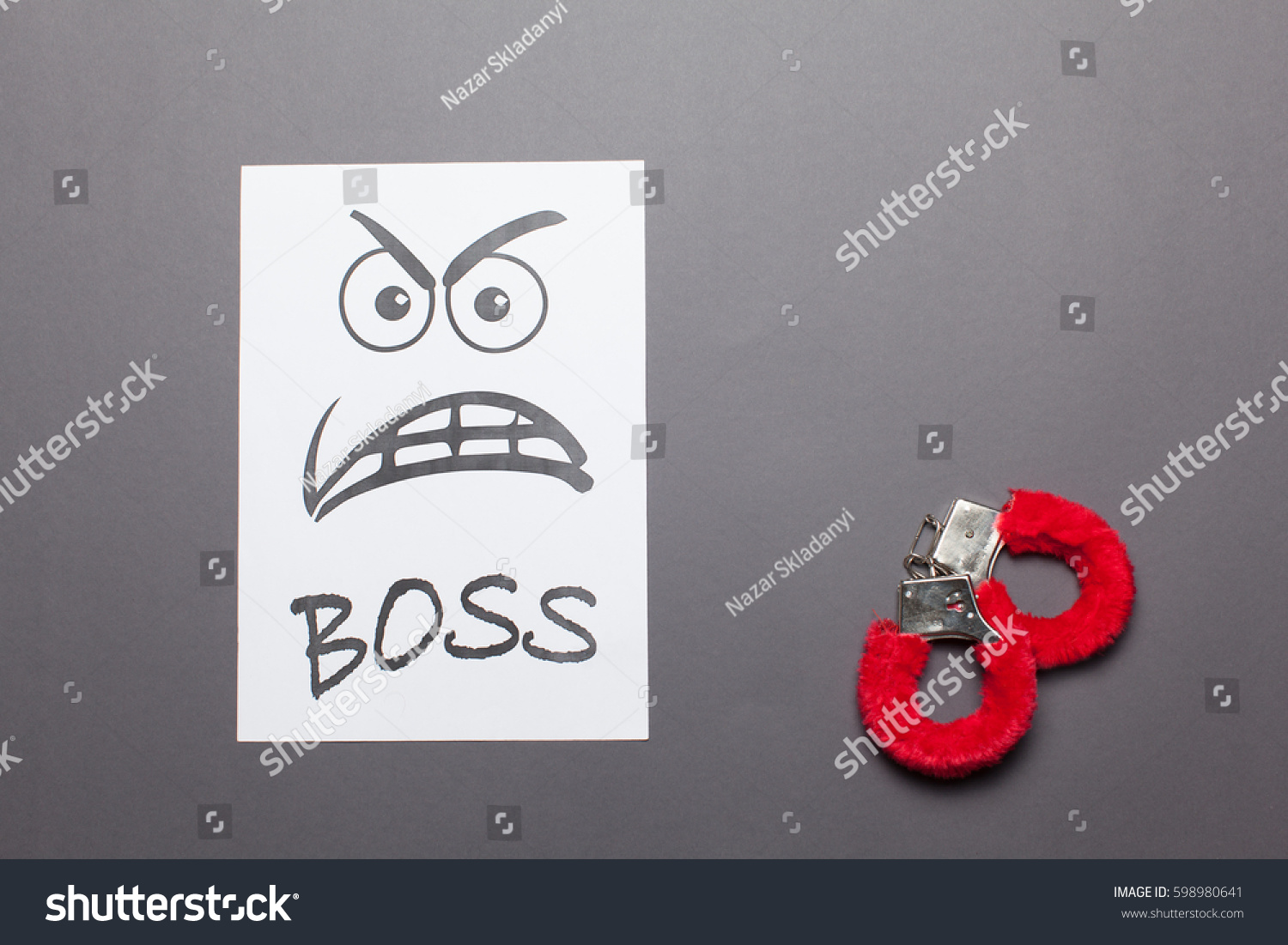  Evil painted boss face with red handcuffs on a white paper  isolated gray background.Sexual harassment concept. #598980641