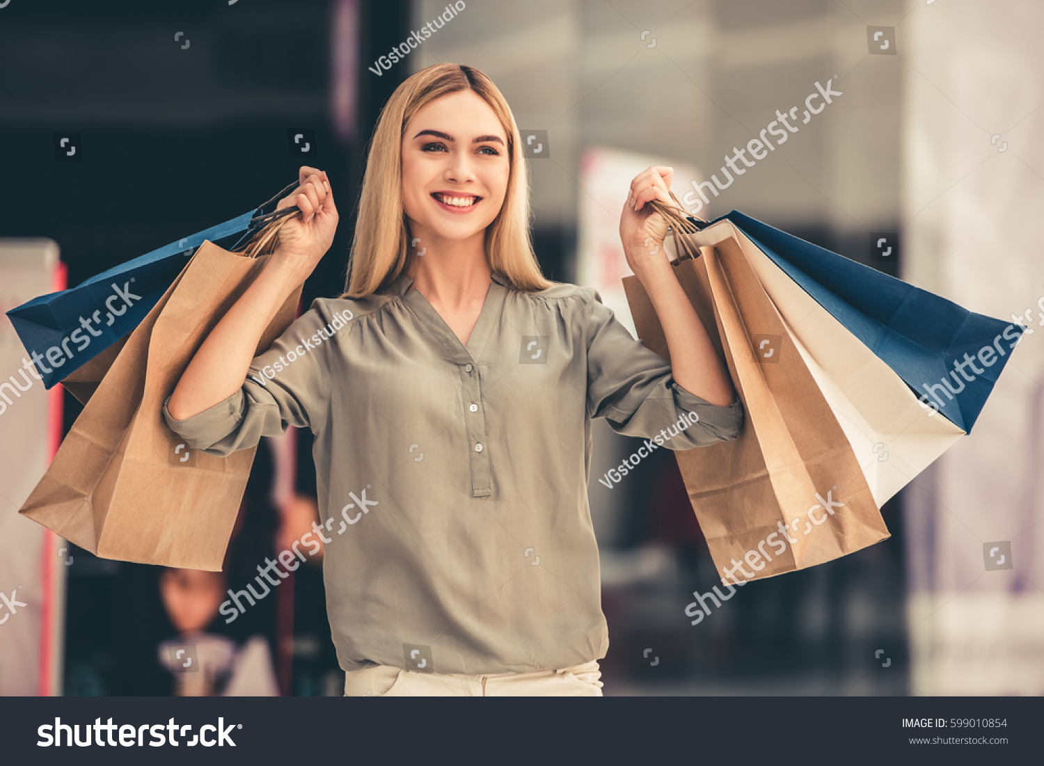 Attractive girl is holding shopping bags, looking at camera and smiling while standing in the mall #599010854