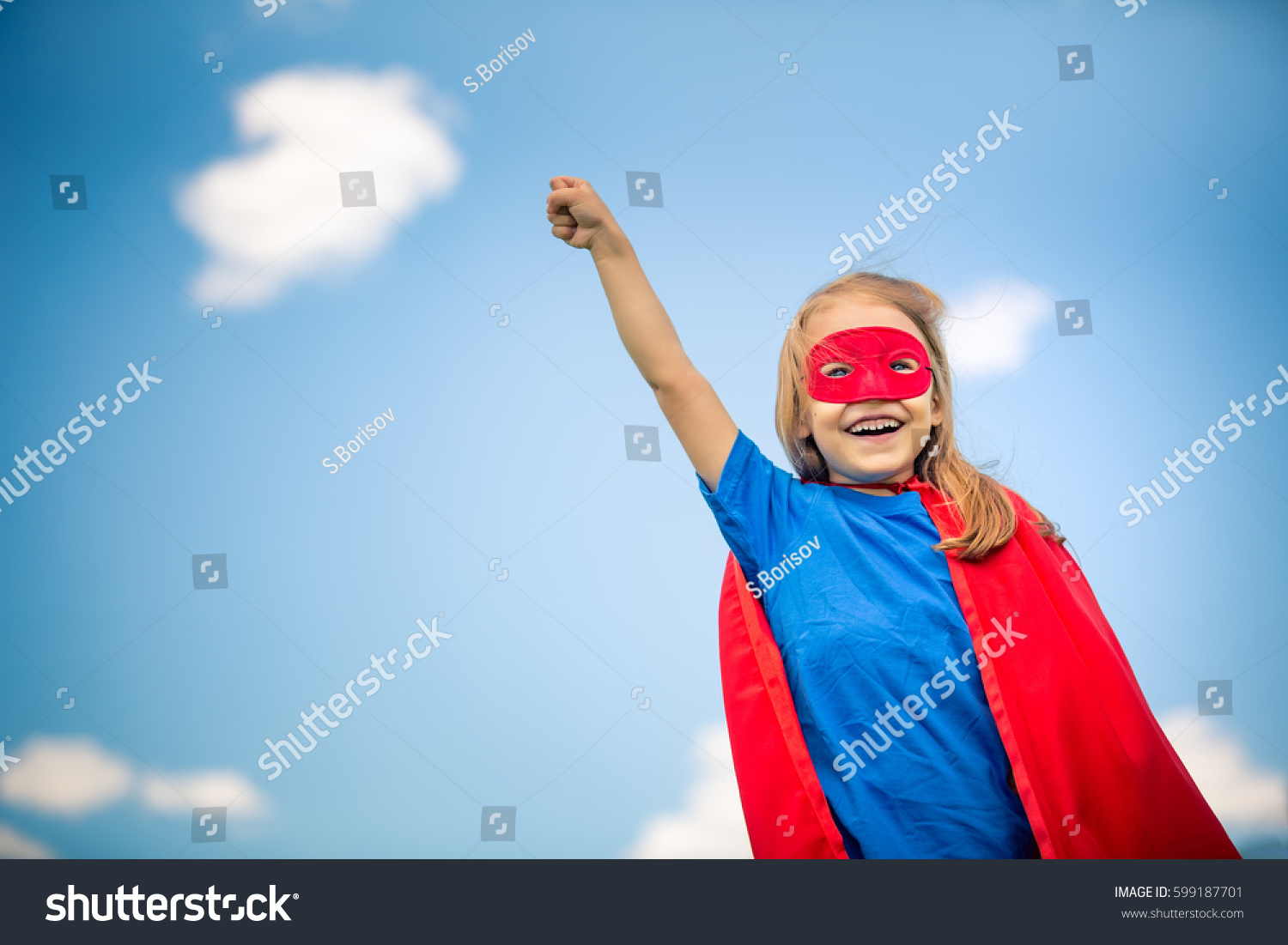 Funny little girl plays super hero over blue sky background. Superhero concept. #599187701