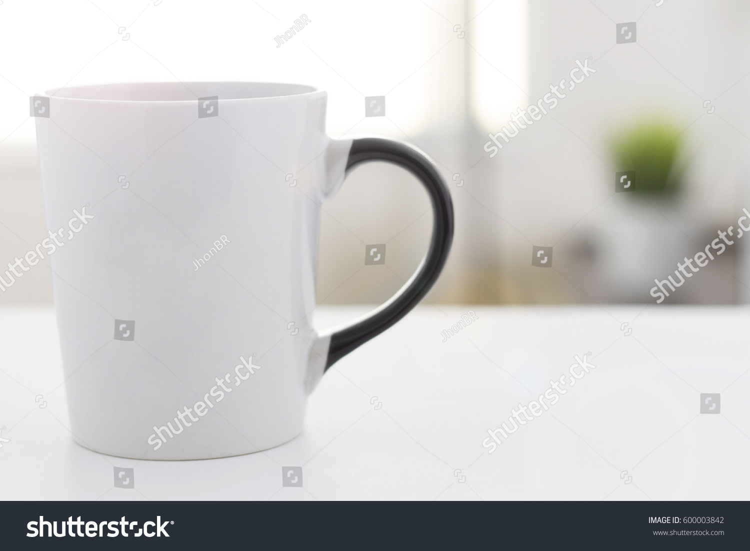 white coffee mug with black handle, on a withe table and blurred background in the morning #600003842
