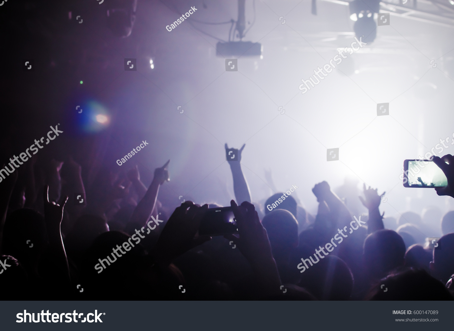 silhouettes of people at a rock festival concert in front of the scene in bright light #600147089