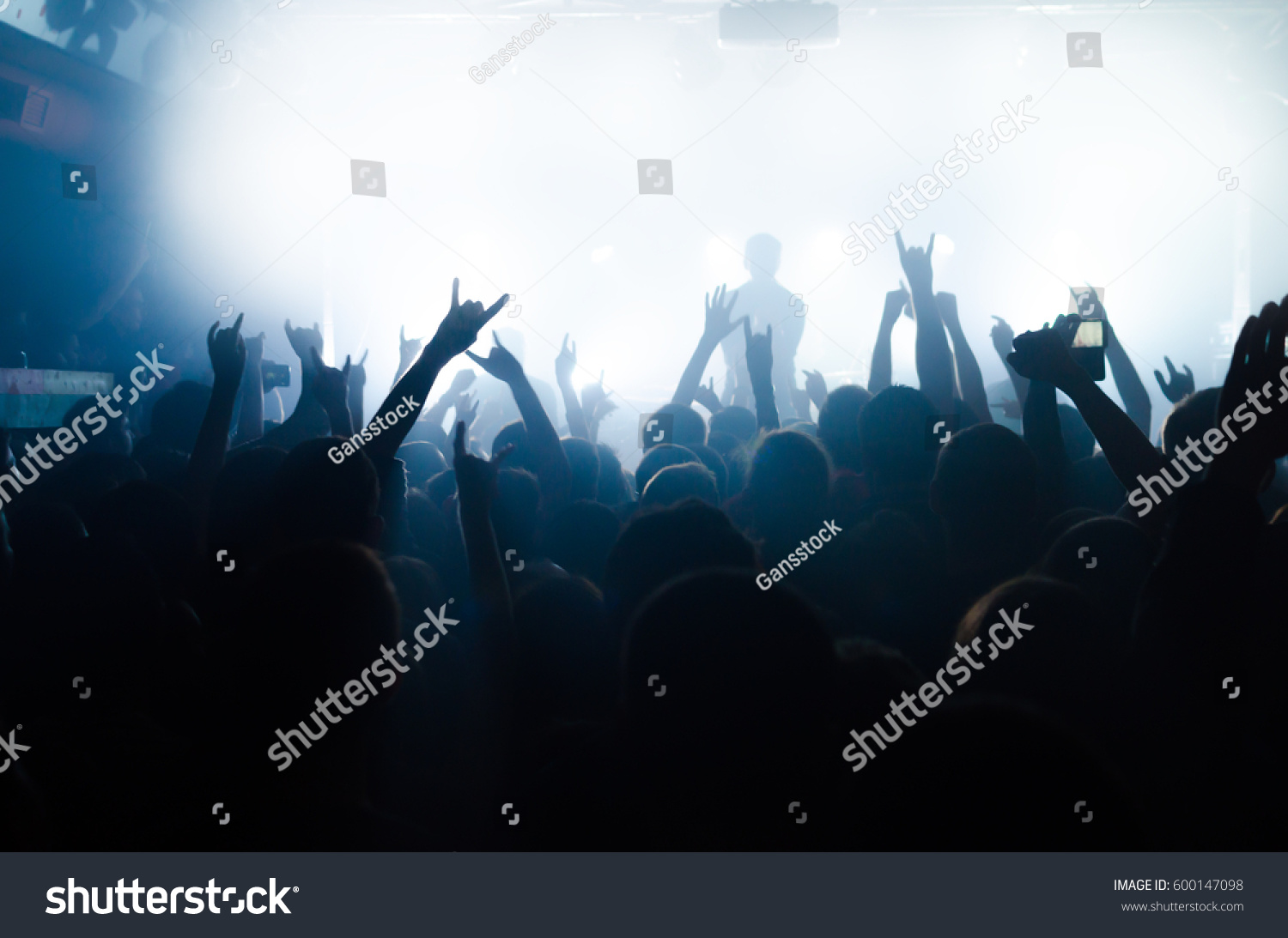 silhouettes of people at a rock festival concert in front of the scene in bright light #600147098