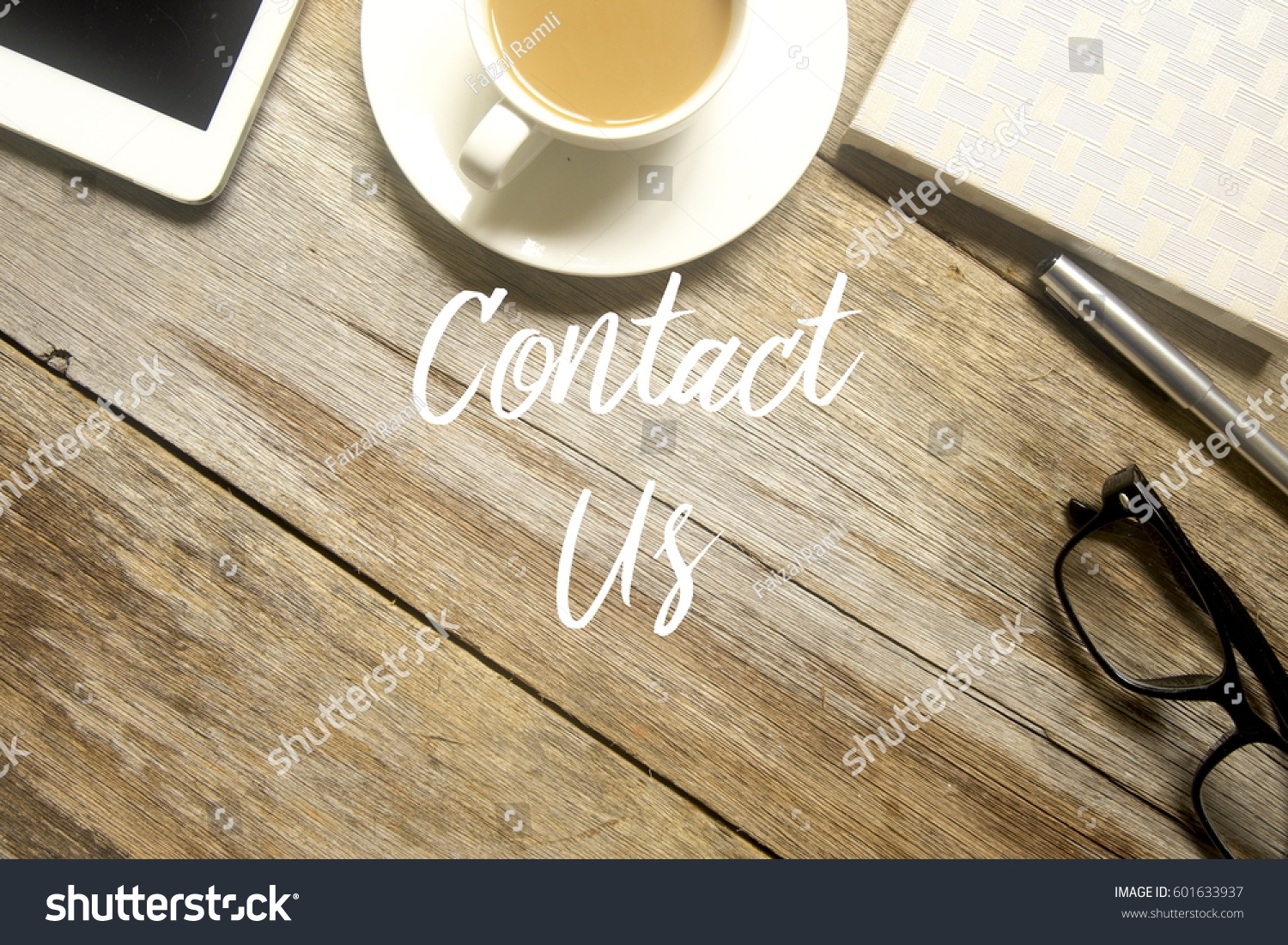 A business concept. A tablet pc, cup of coffee, glasses, pen and notebook with CONTACT US written on wooden table. #601633937