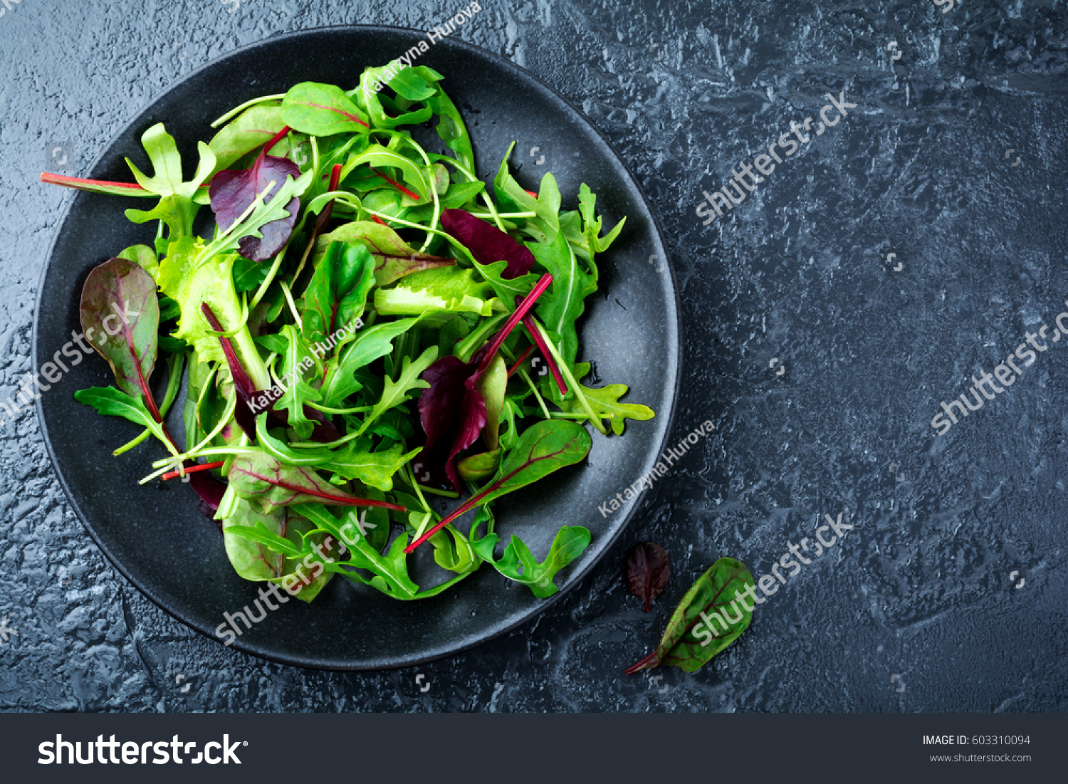 Mix fresh leaves of arugula, lettuce, spinach, beets for salad on a dark stone background. Selective focus. #603310094
